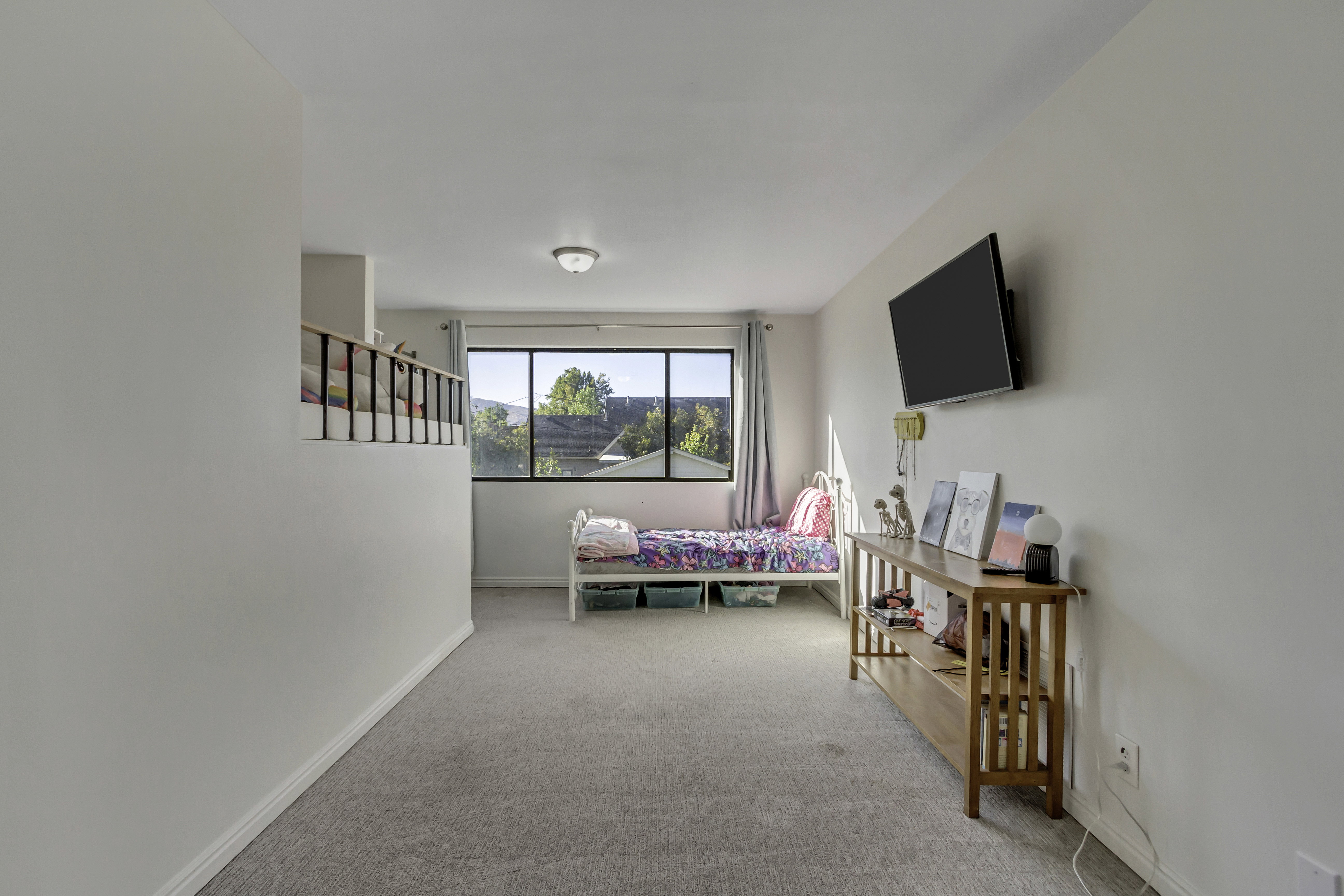 Carpeted room featuring a large window with exterior views, a built-in wall partition with railing, and a flush-mount ceiling light fixture