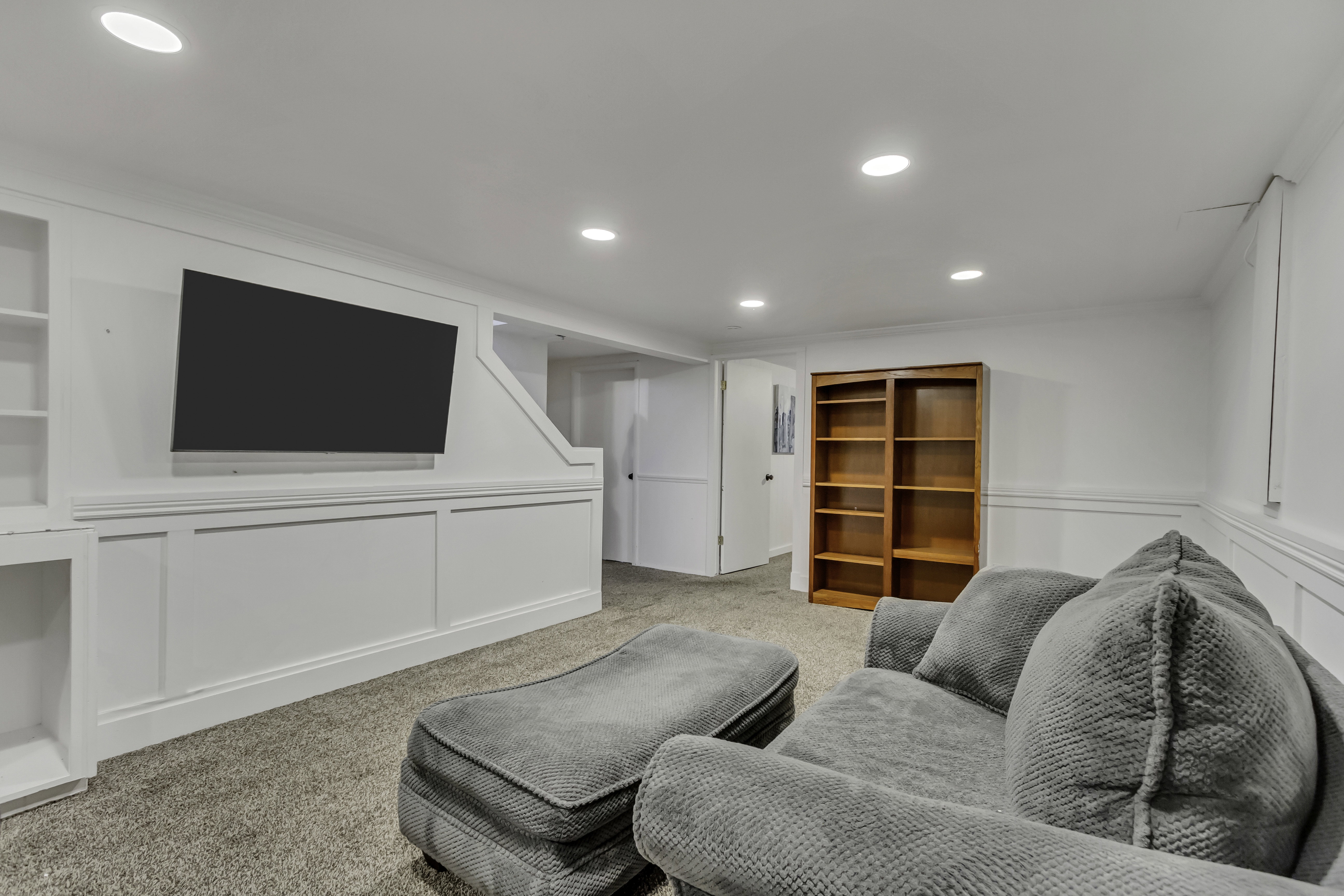 Recessed lighting illuminates this space featuring wall paneling and built-in shelving