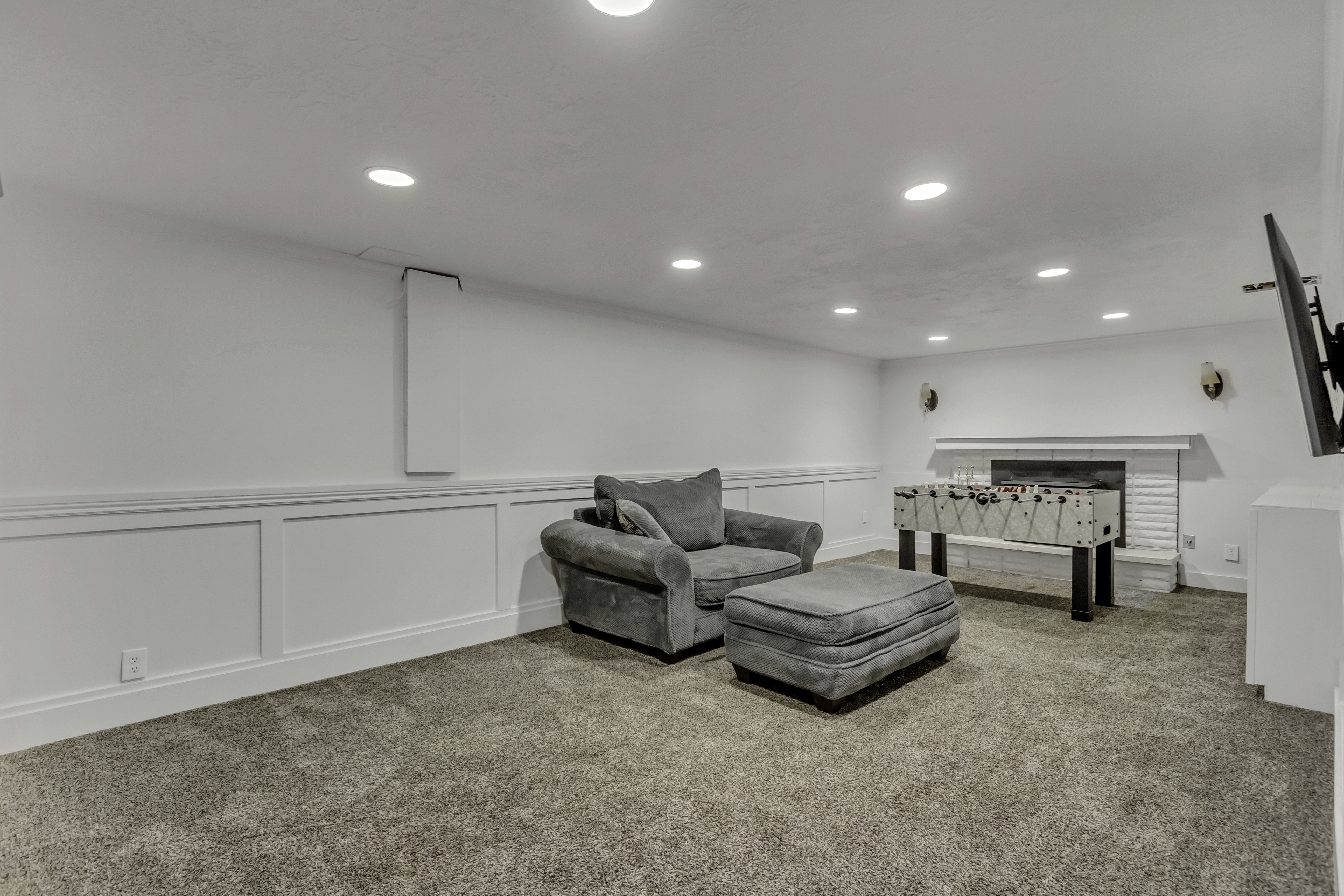 Recessed lighting illuminates this carpeted room featuring white panel wainscoting