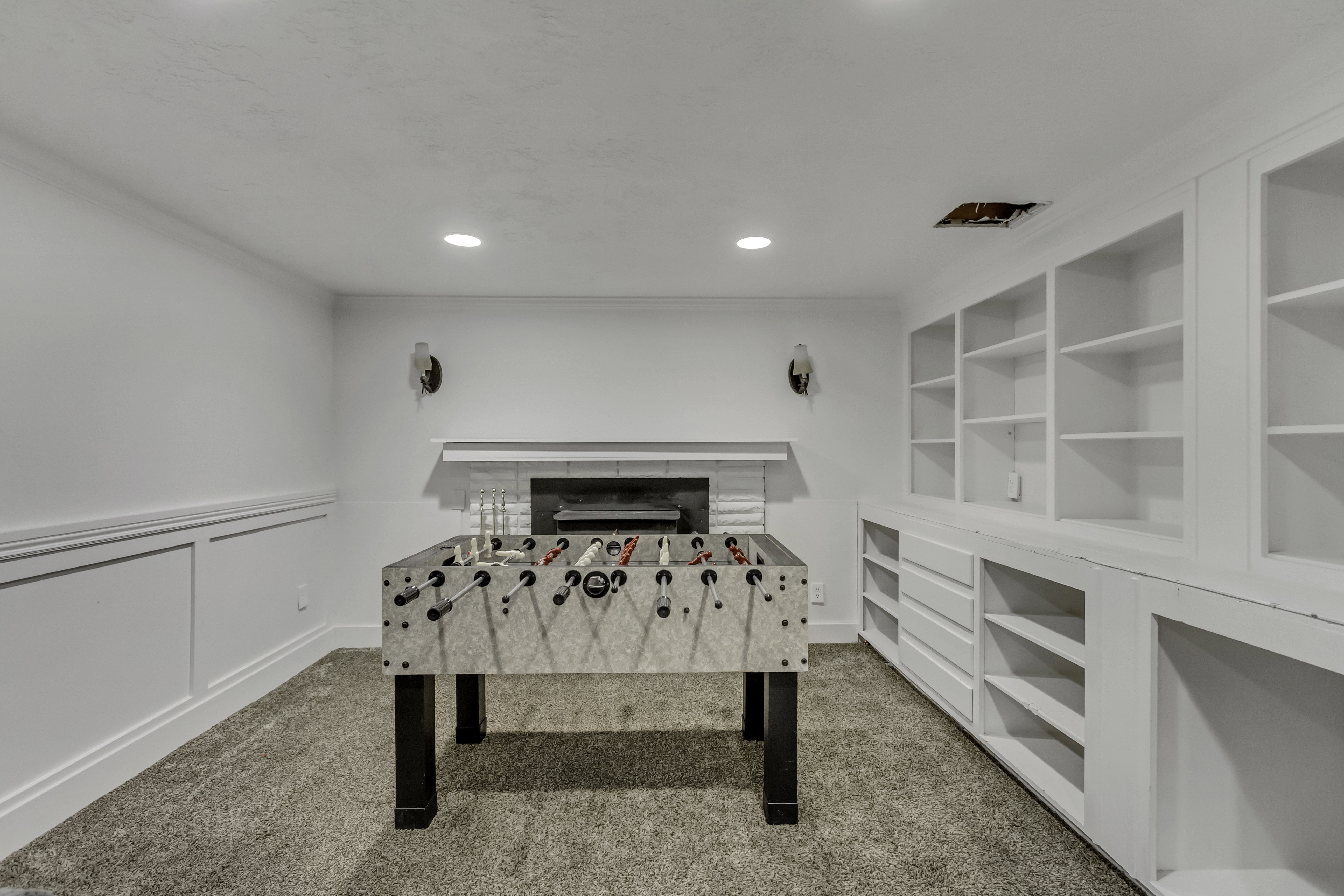 Finished room featuring recessed lighting, wall sconces, a fireplace with a white mantel, white wainscoting, and built-in shelving with integrated drawers