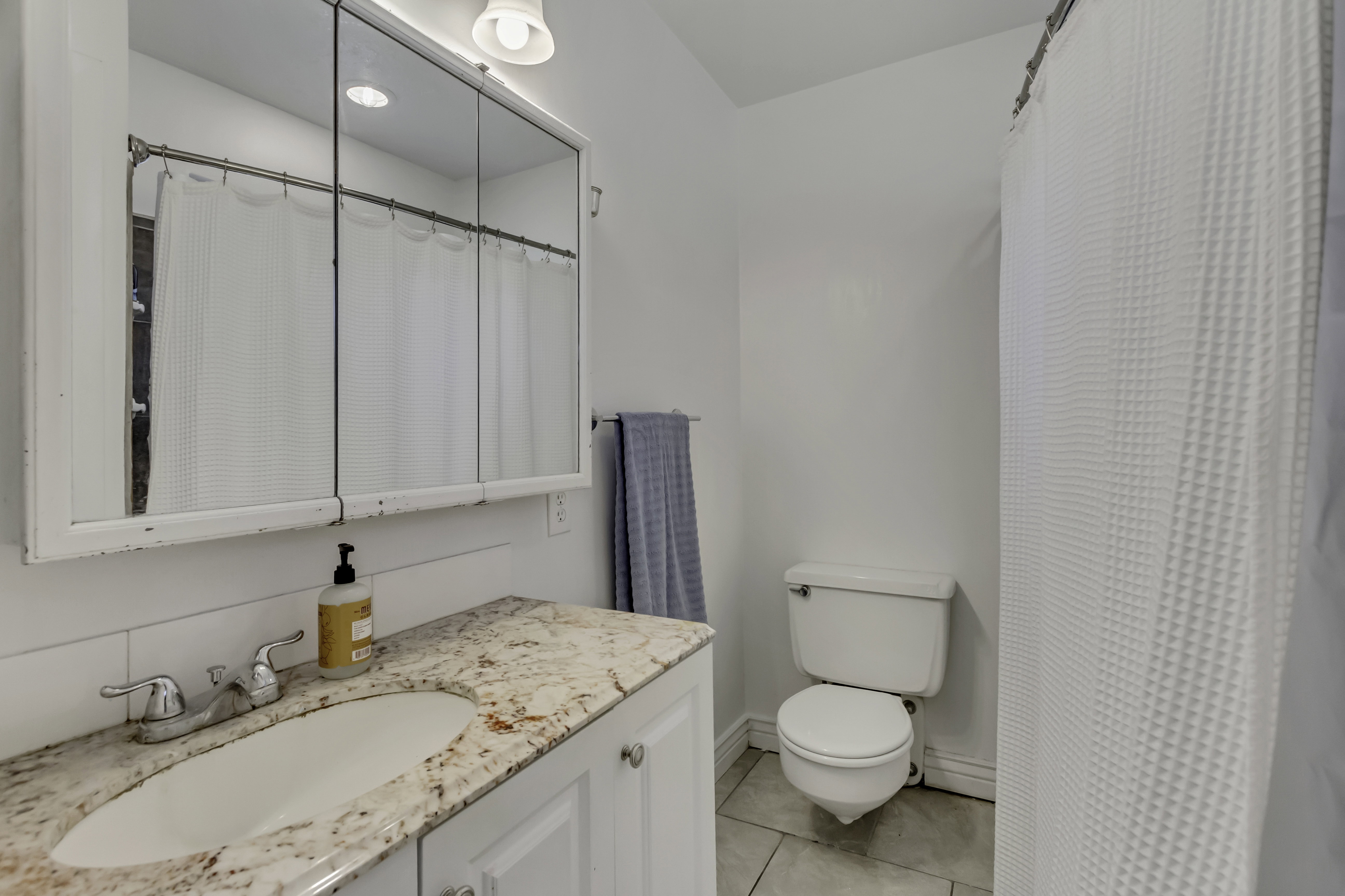 Bathroom featuring a vanity with an integrated sink and patterned countertop, a triple-door medicine cabinet, and a toilet
