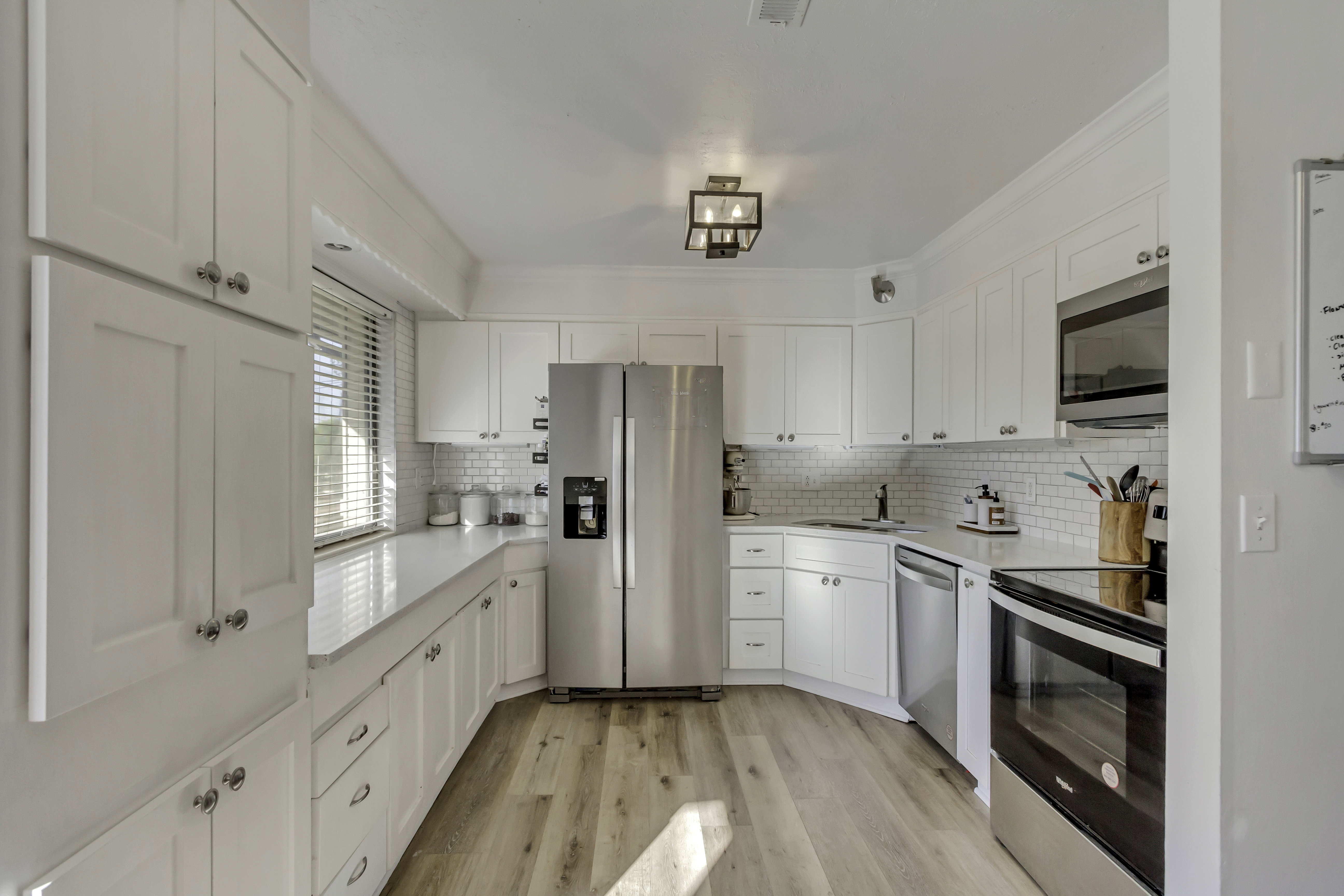 Modern kitchen featuring white shaker cabinetry, stainless steel appliances, light wood-finish flooring, subway tile backsplash, and white countertops
