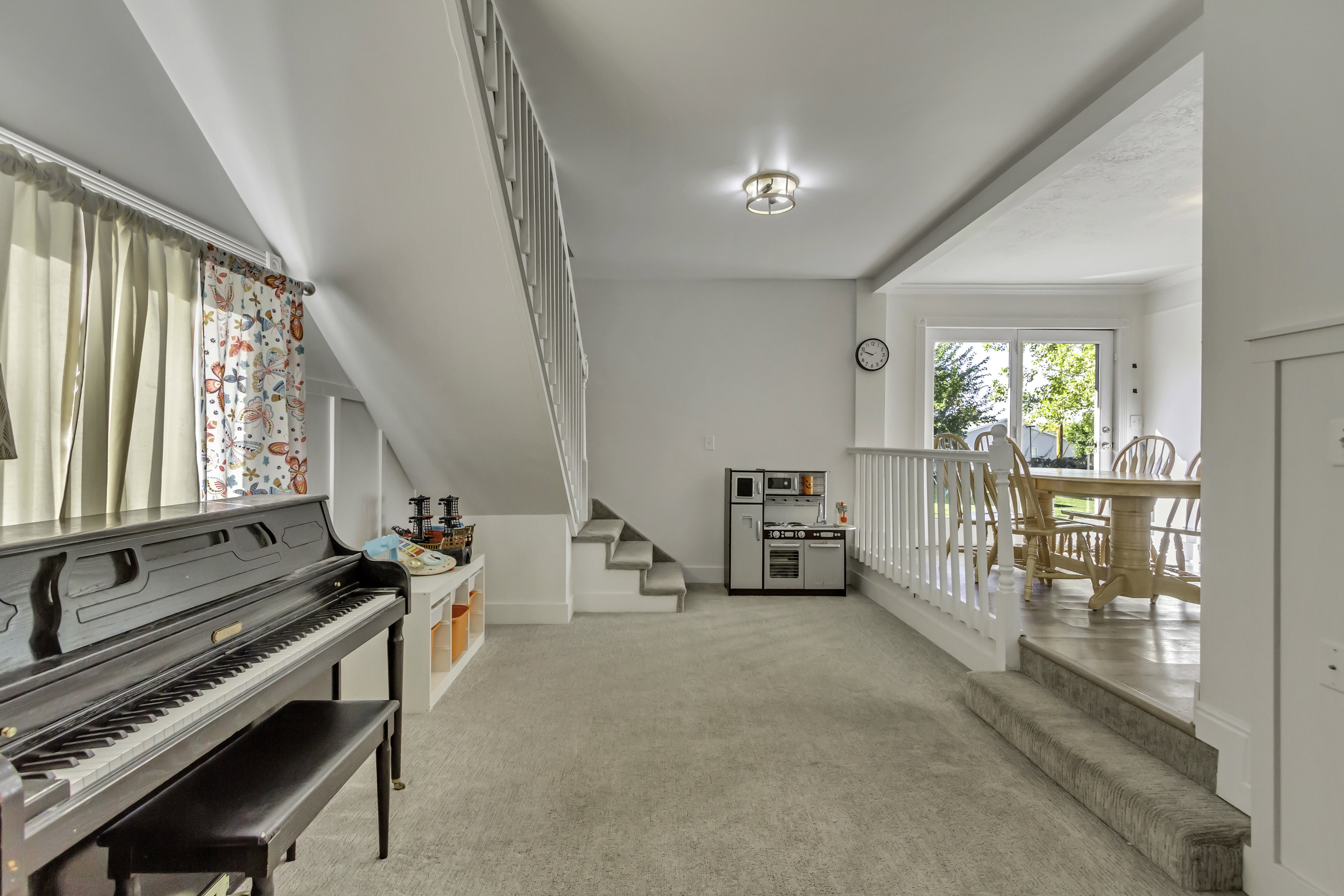 Carpeted lower level with white walls and a staircase featuring a white railing