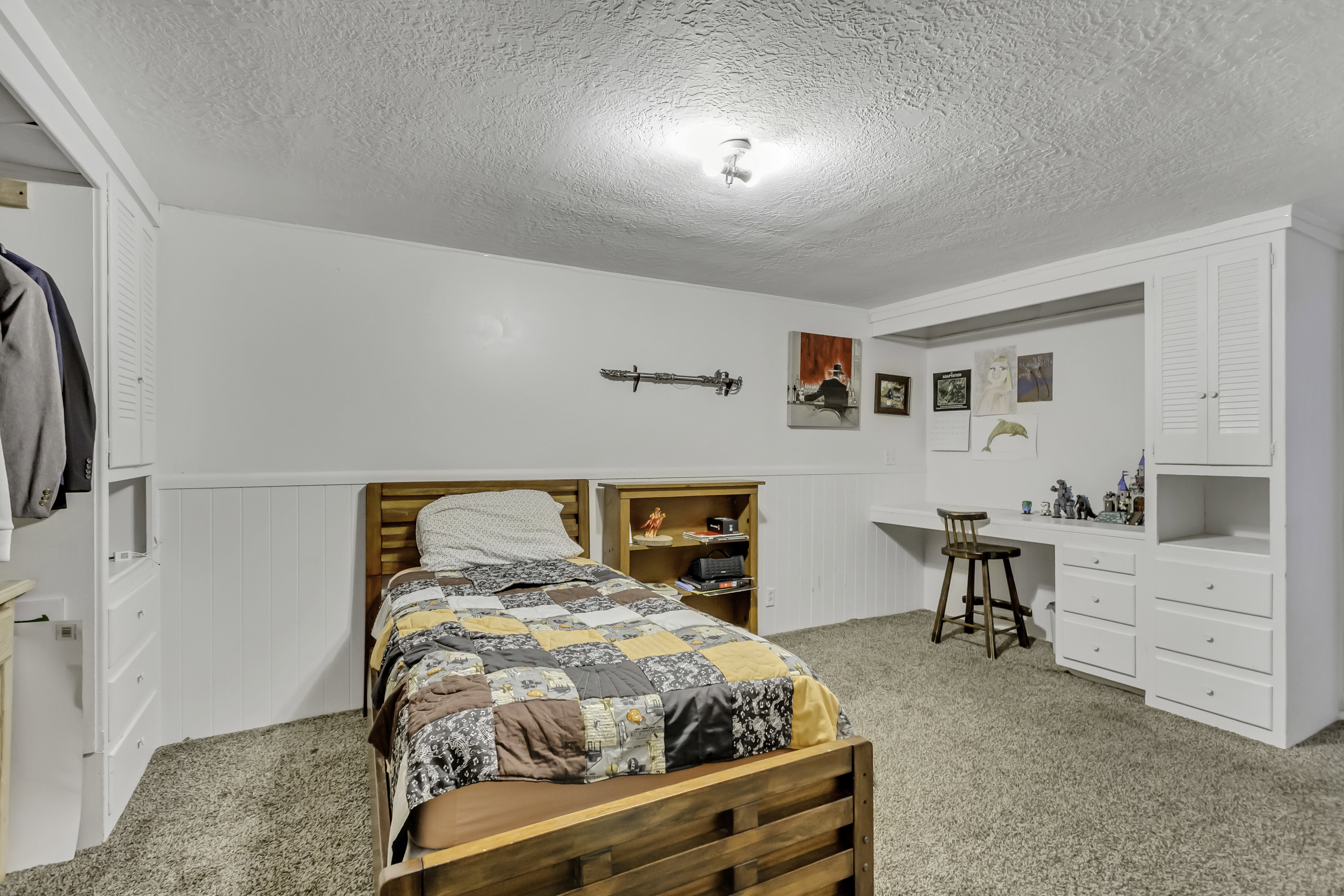 Room featuring white wainscoting, built-in desk, built-in cabinetry with louvered doors, built-in shelving, and carpet flooring