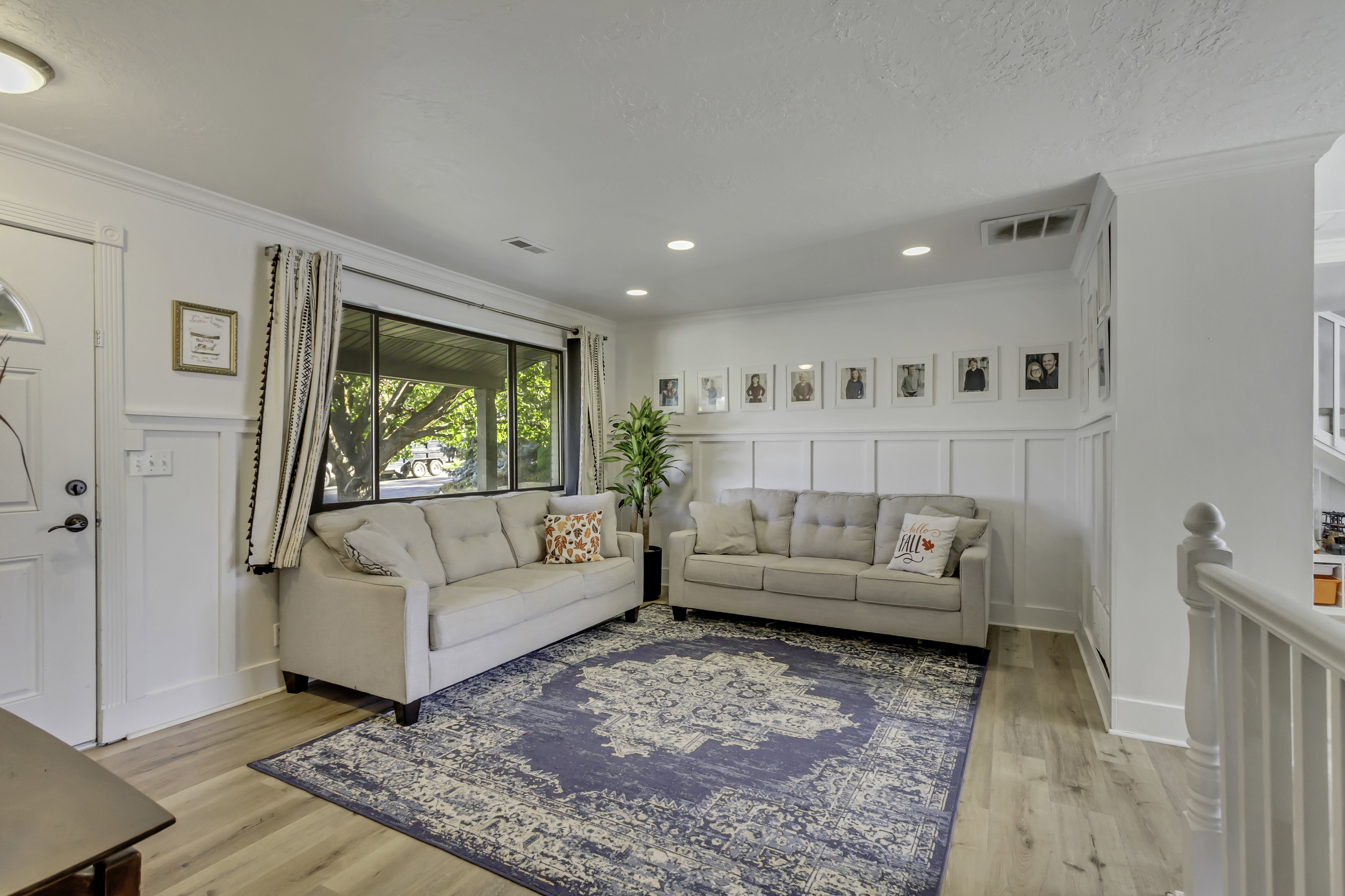 Bright living area featuring wood-finish flooring, white board and batten wall detailing, and a large picture window