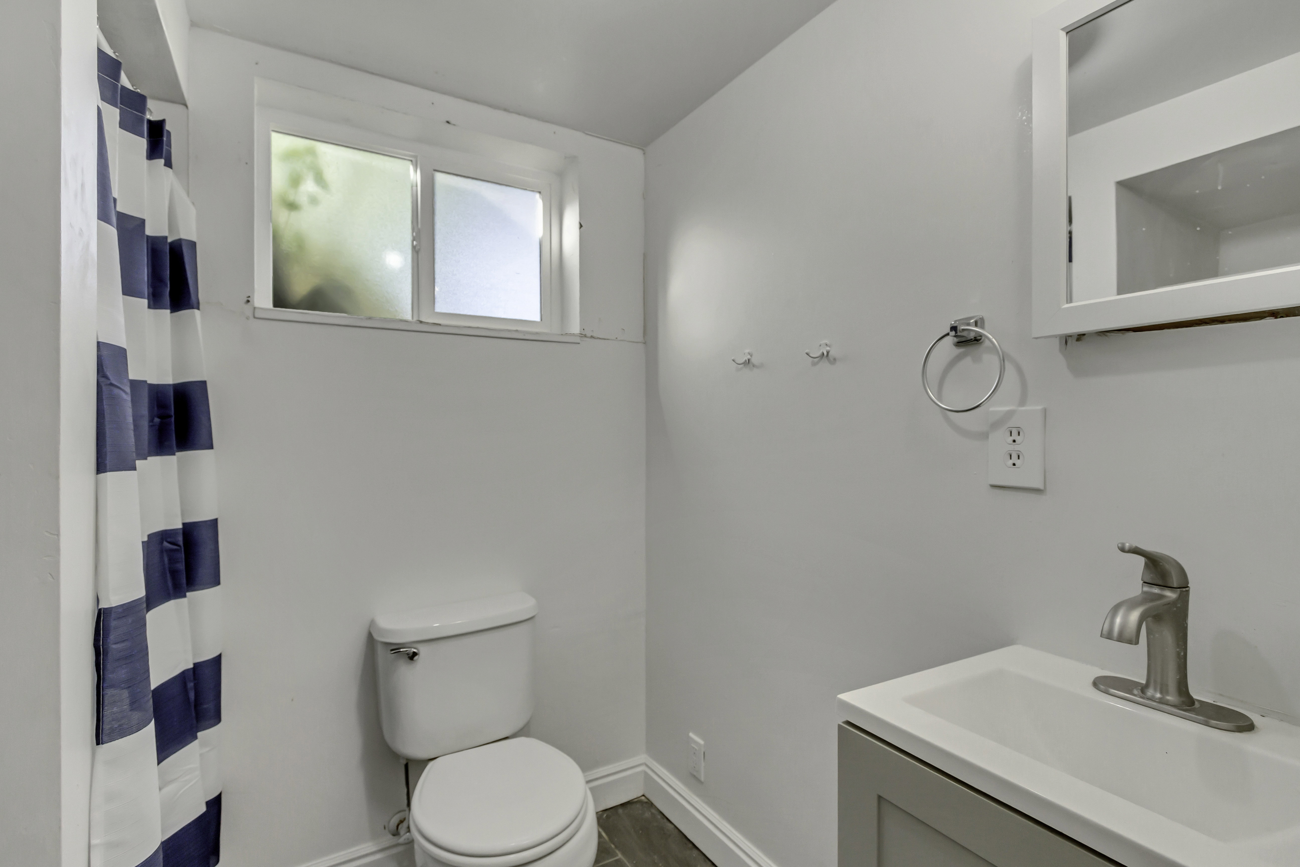 Compact bathroom featuring a window, toilet, and vanity with an integrated sink
