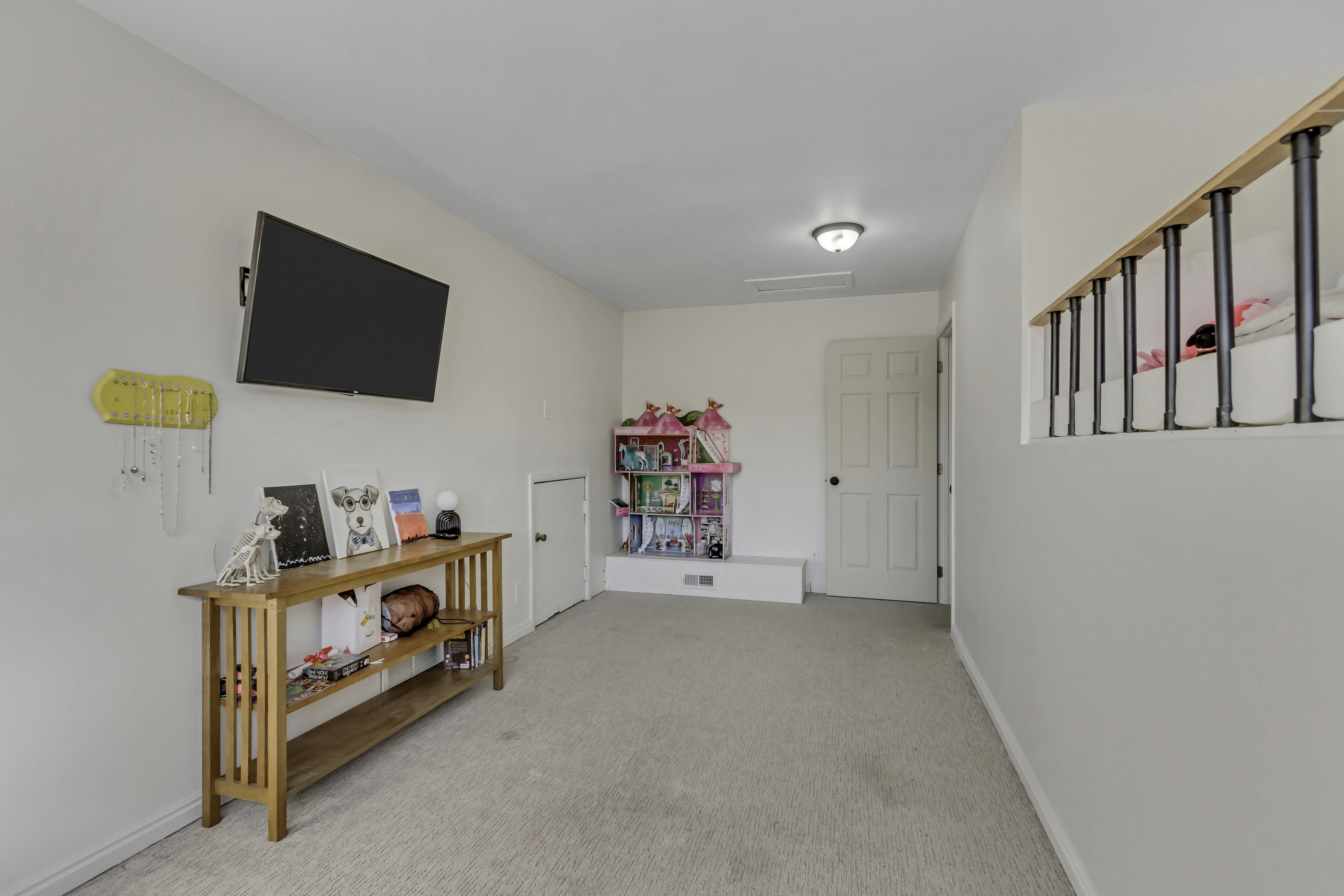 Carpeted bonus room with a light fixture, single panel doors, and a banister featuring black balusters and a wood-finish handrail
