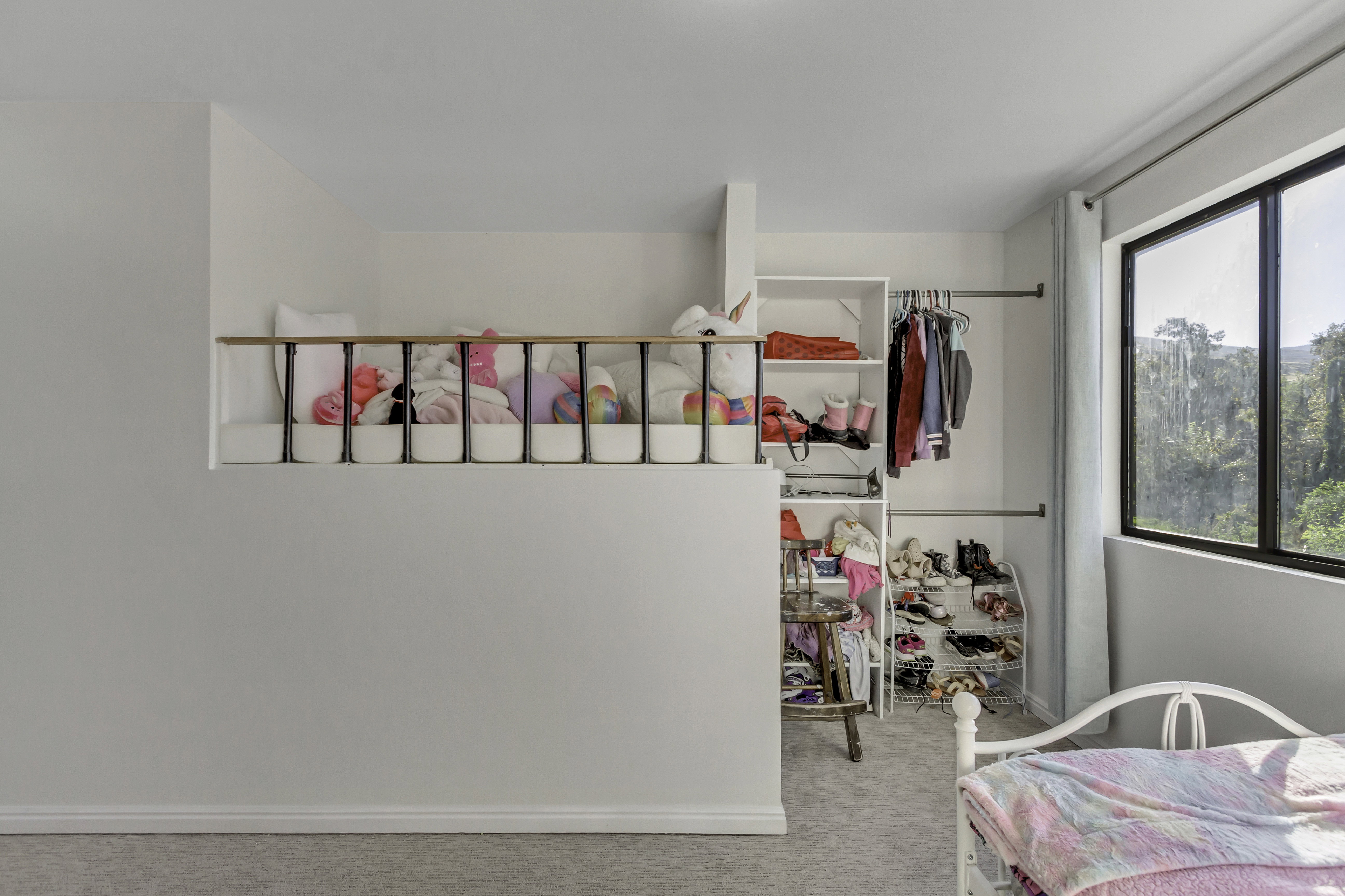 Bright interior with a built-in storage loft, integrated shelving, and a large window offering expansive tree-lined scenery