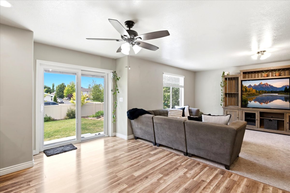 Living area featuring wood-finish flooring, a ceiling fan with integrated lighting, and a large sliding glass door opening to the backyard