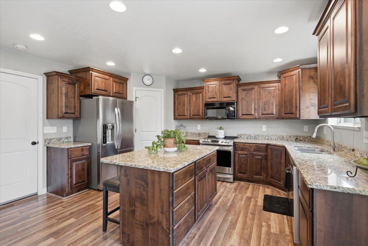 Spacious kitchen featuring wood-finish flooring, recessed lighting, a central island with countertop seating, stainless steel appliances, and ample cabinetry