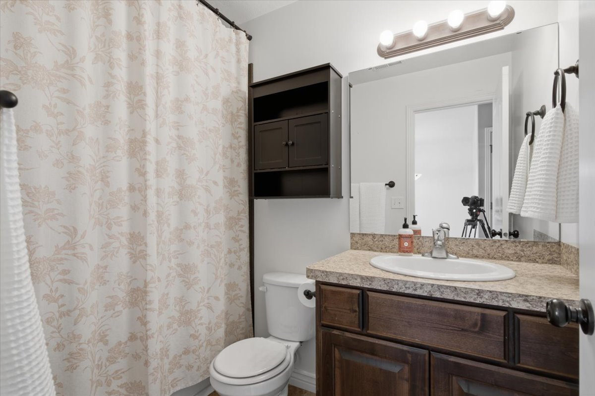 Bathroom featuring a dark wood-finish vanity with a light speckled countertop, an undermount sink, and a framed mirror