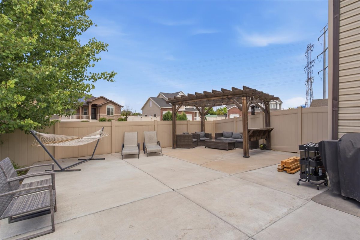 Expansive concrete patio featuring a wood pergola, built-in bar, and perimeter fencing