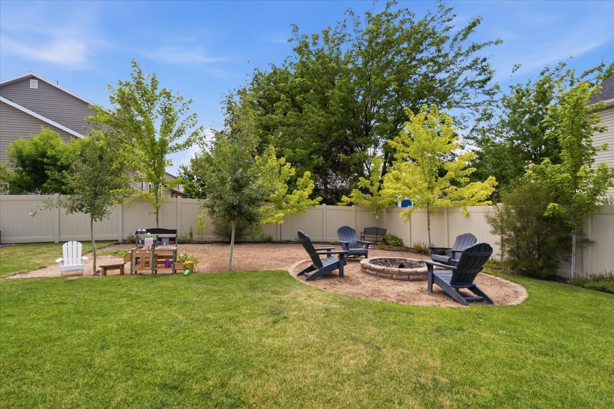 Expansive backyard featuring a stone-lined fire pit area, mature trees, and a perimeter privacy fence