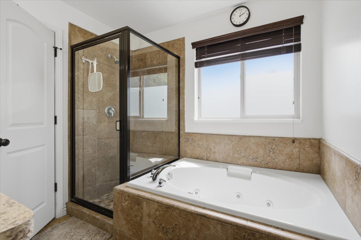 Bathroom featuring a jetted soaking tub, a glass-enclosed shower with tiled walls, and a window with wood-finish blinds