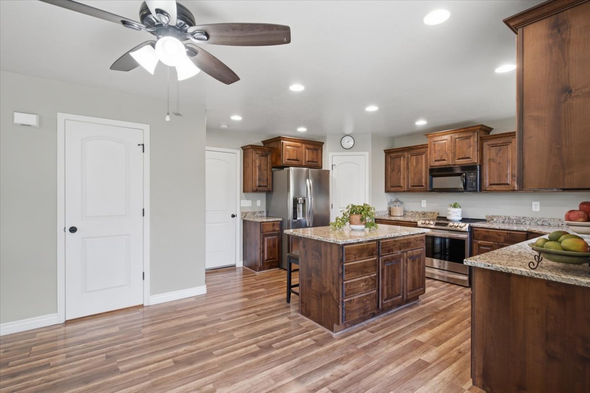 Spacious kitchen featuring a central island with granite countertop, abundant wood cabinetry, stainless steel appliances, and wood-finish flooring