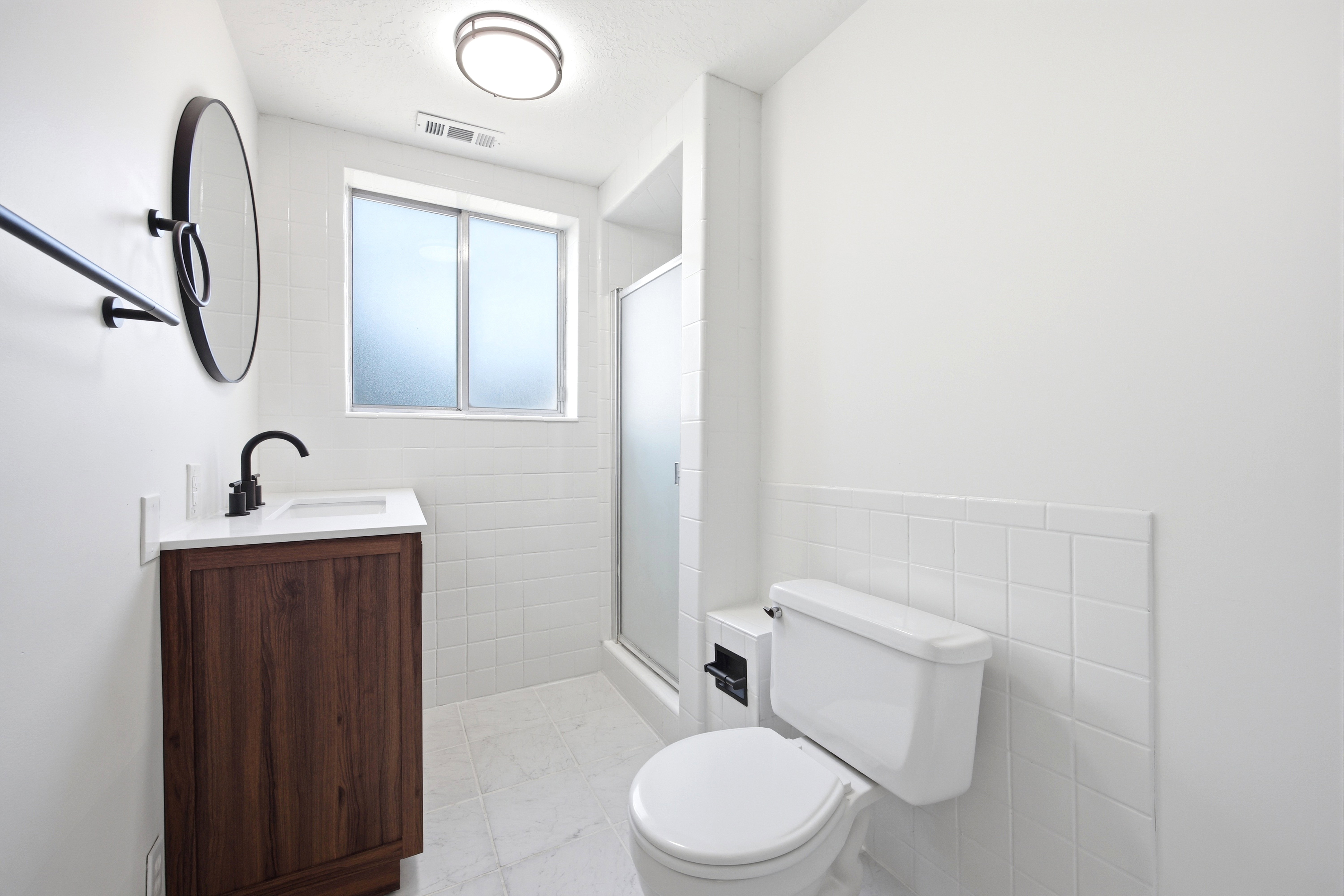 Bathroom featuring a dark wood-finish vanity with a white countertop and matte black faucet, white subway tile wainscoting, and a frosted glass window