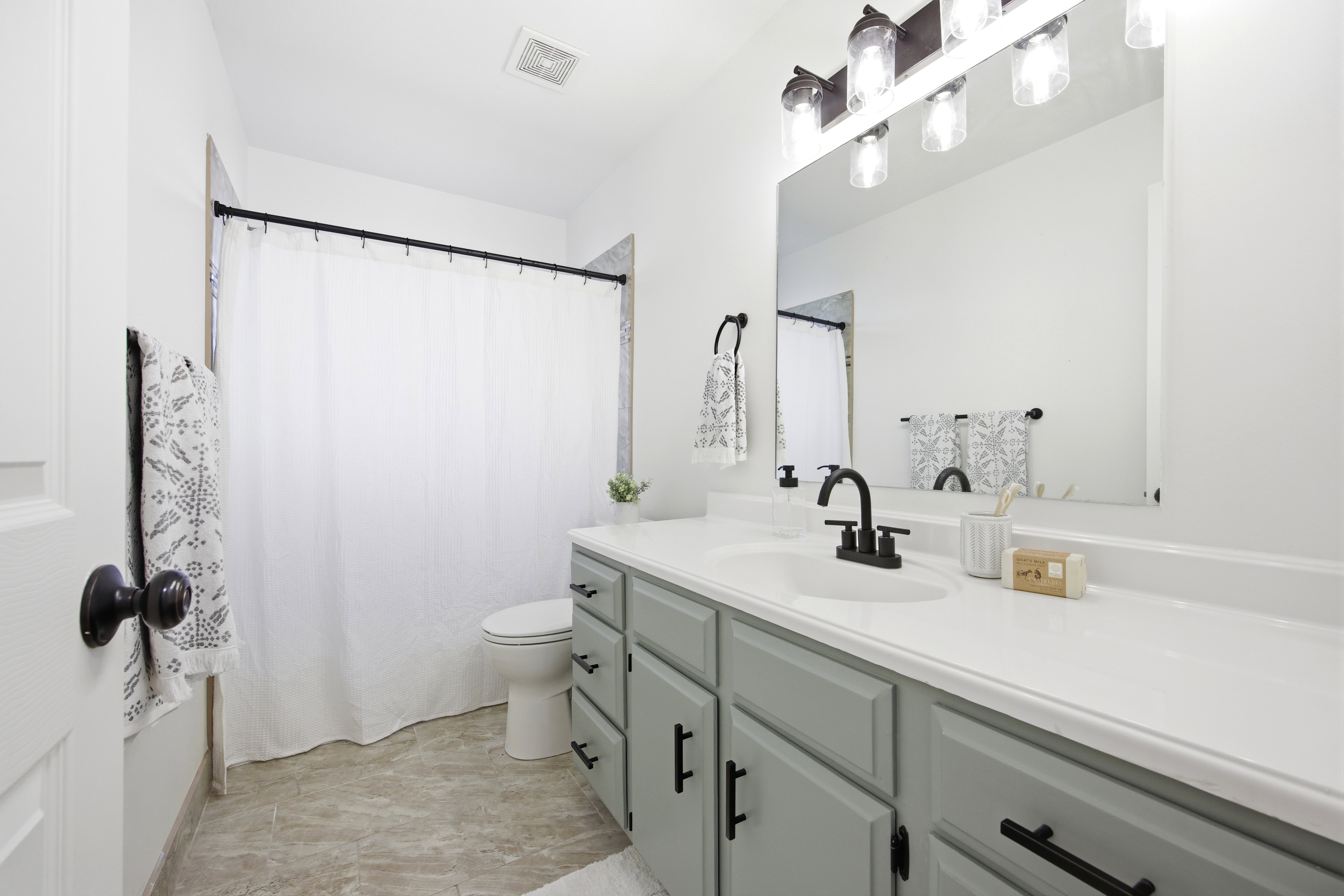 Bathroom featuring a spacious vanity with a white countertop, a black matte faucet, and light gray cabinetry with black hardware