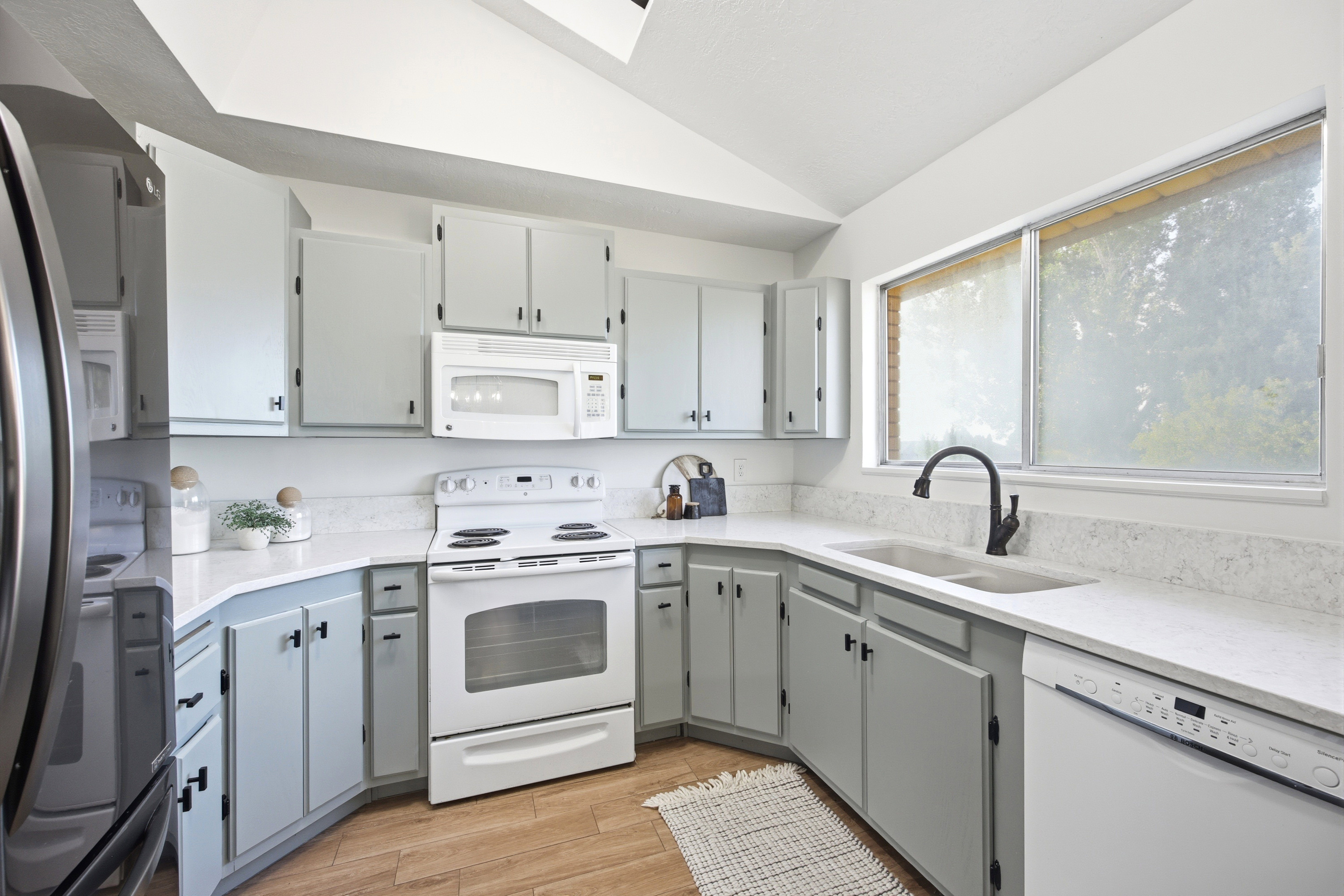 Bright kitchen featuring light-toned cabinetry, light countertops, wood-finish flooring, and a double basin sink with a matte black faucet