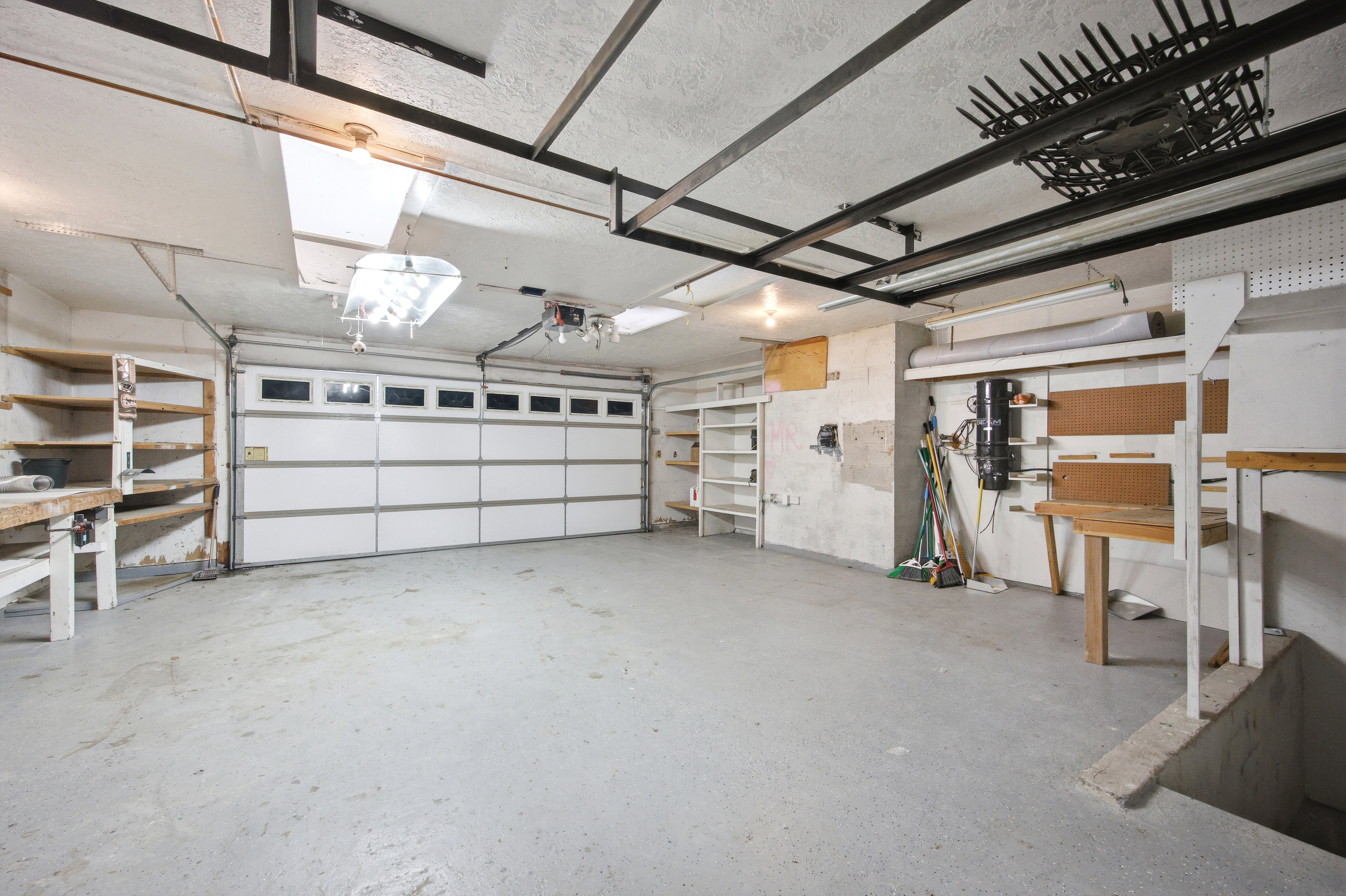 Spacious garage featuring a sectional overhead door with windows, concrete flooring, and exposed ceiling joists