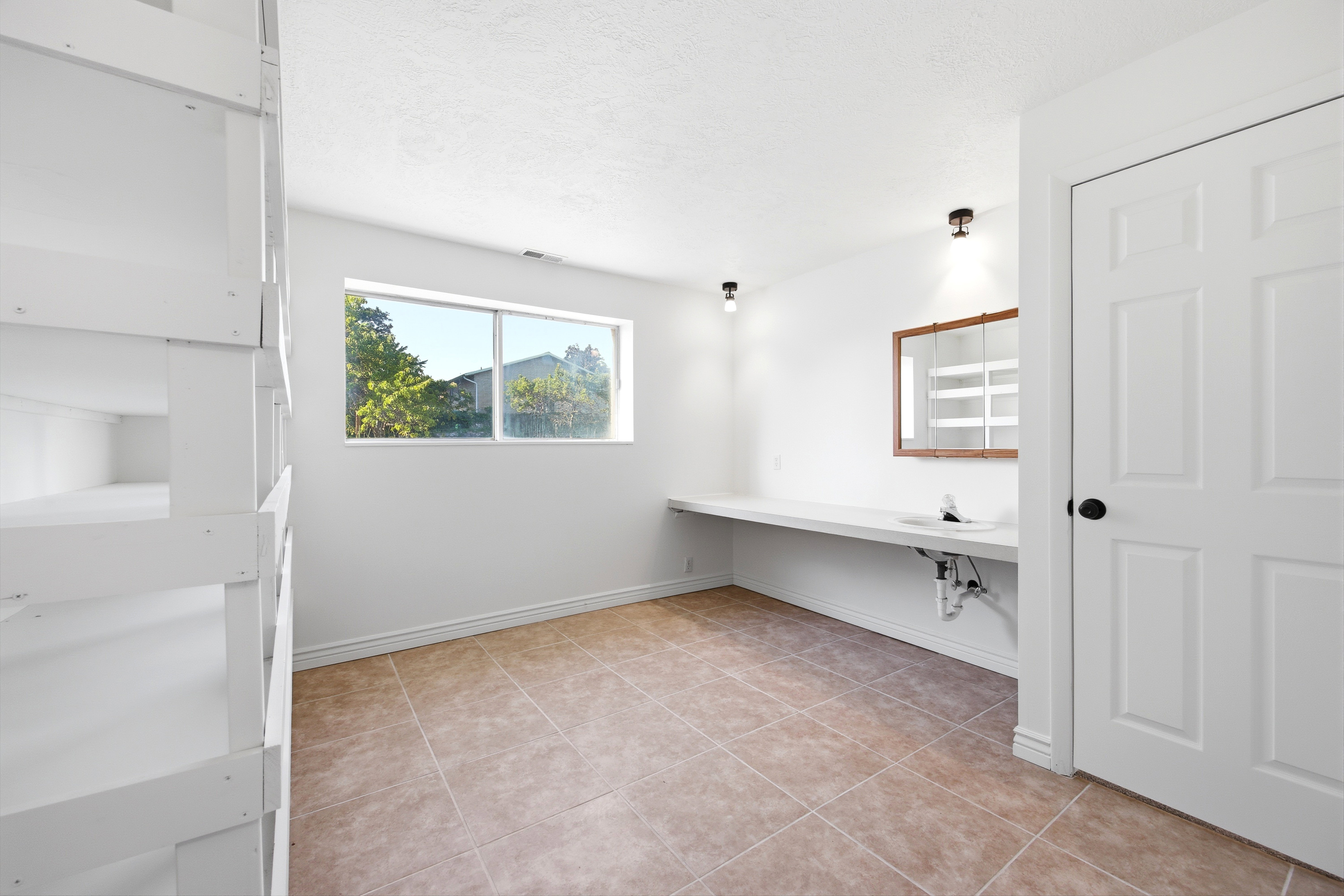 Bright room with natural light, featuring a built-in countertop with an integrated sink, a wall-mounted mirror with wood-tone frame, and overhead lighting fixtures