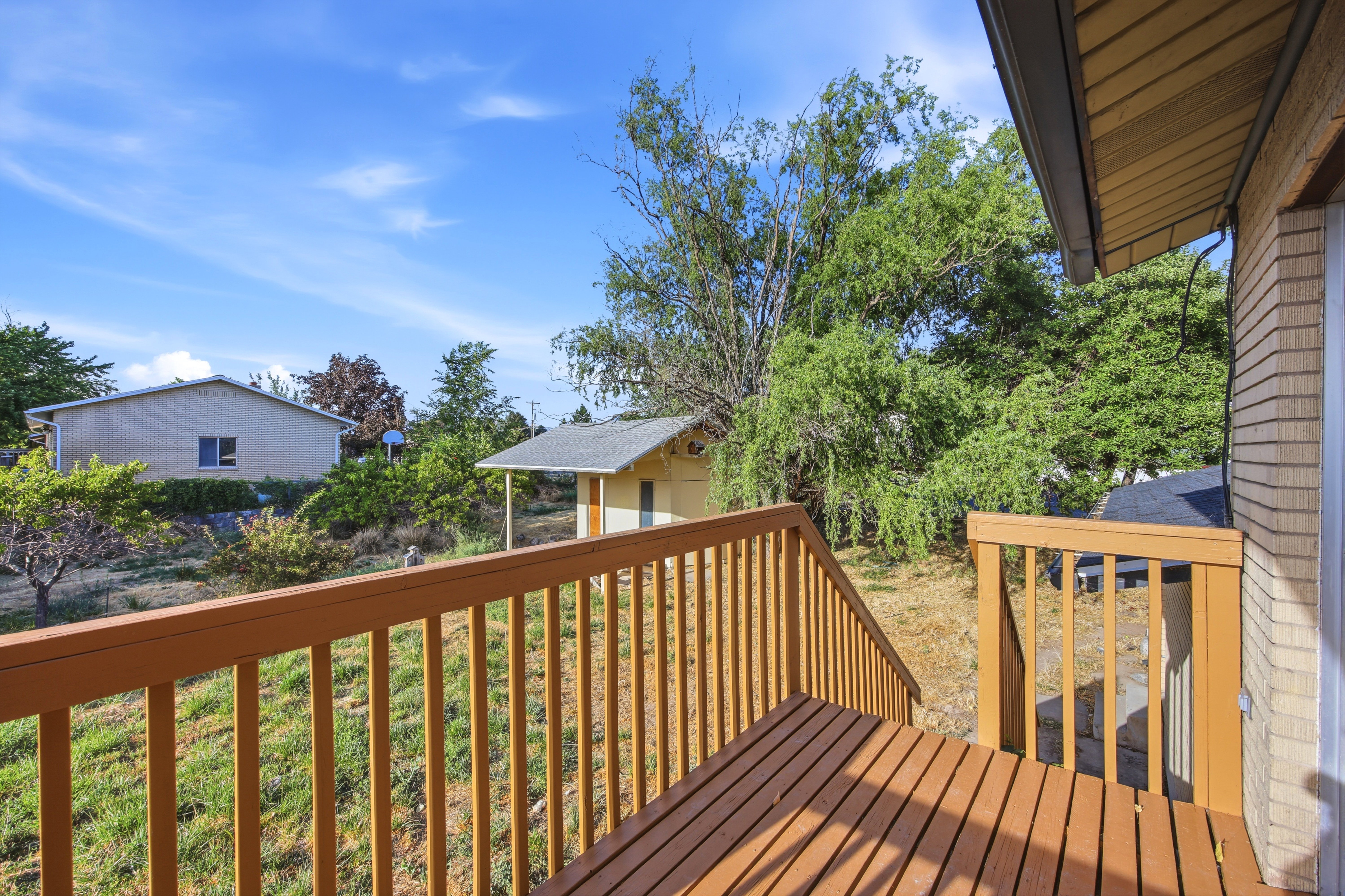 Outdoor deck featuring wood-finish decking and railing, with a partial view of a detached shed and surrounding landscaping