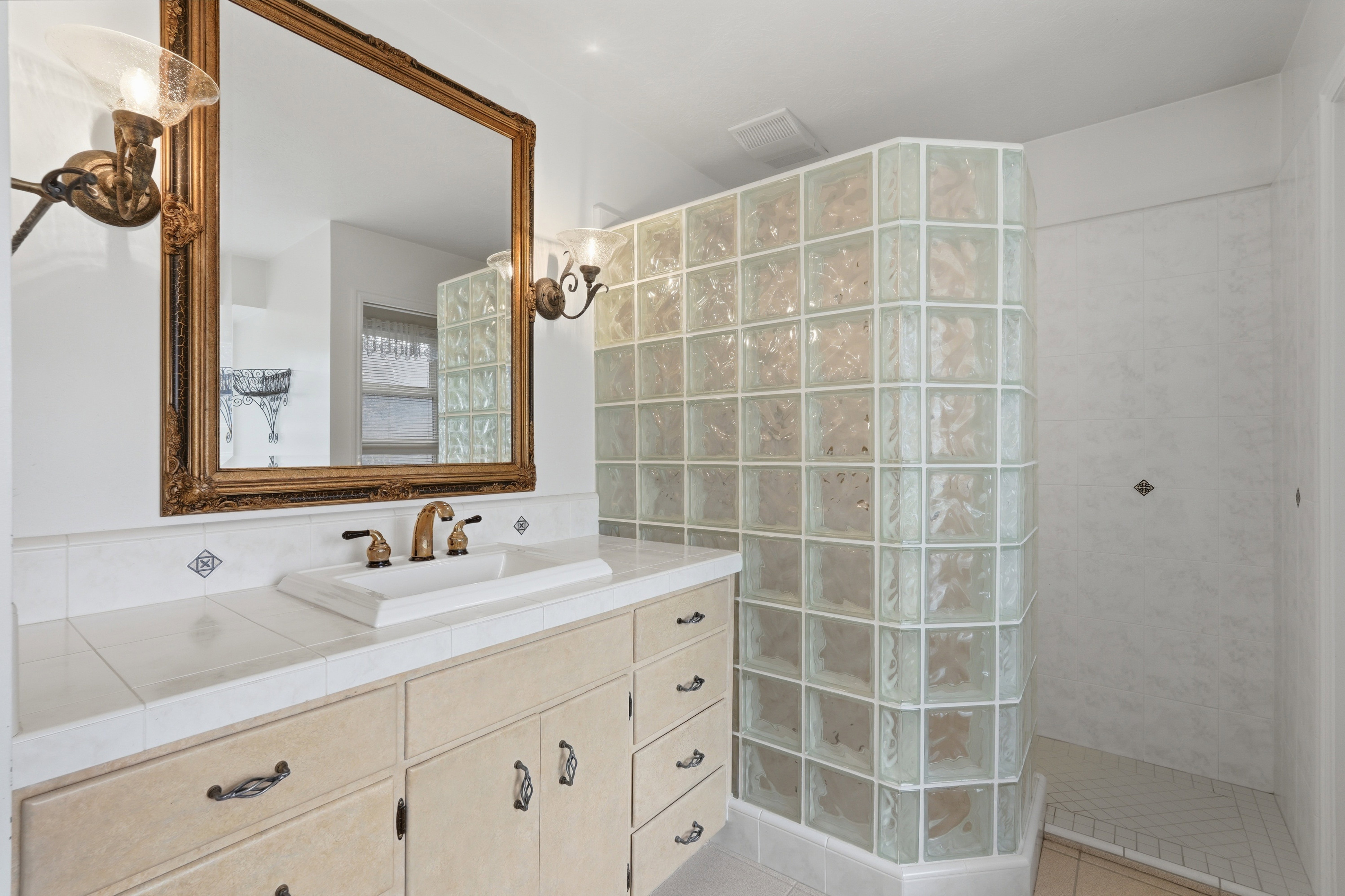Bathroom vanity with an ornate framed mirror, dual sconce lighting, an undermount sink, and a tiled countertop