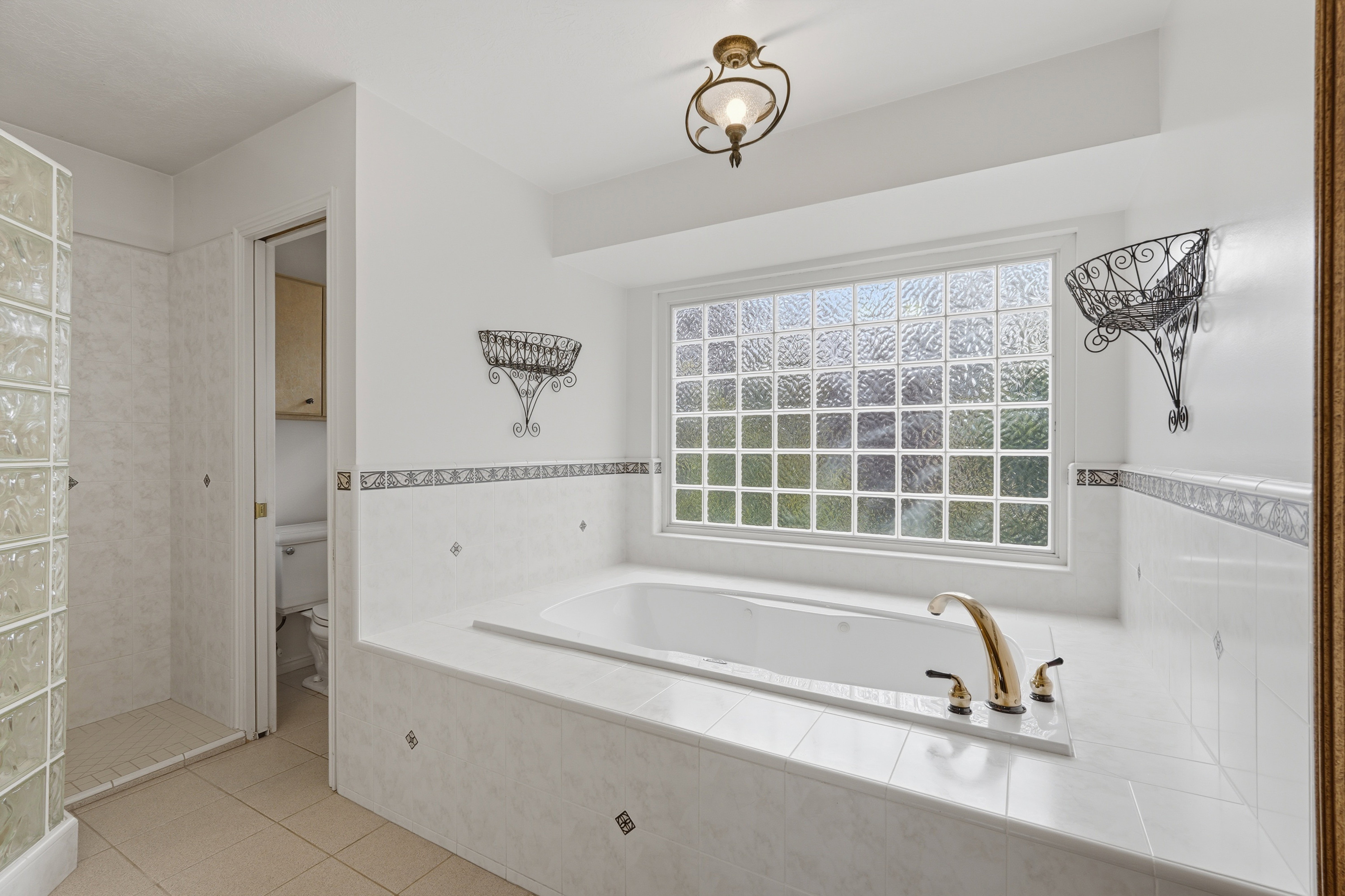 Spacious bath featuring an oversized soaking tub with brass fixtures, a large glass block window, and a separate glass block shower enclosure