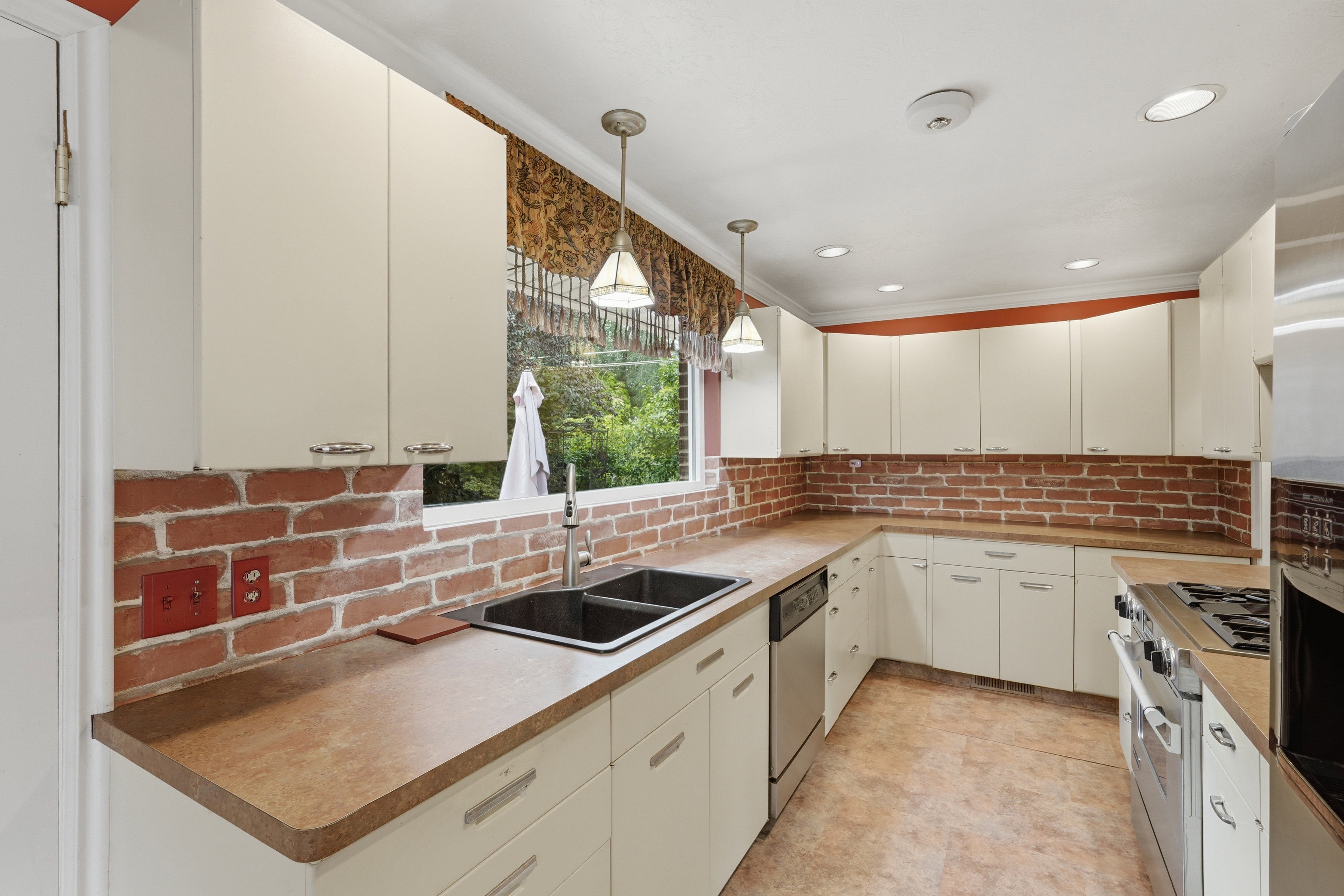 U-shaped kitchen featuring white cabinetry, brick backsplash, and a double basin sink