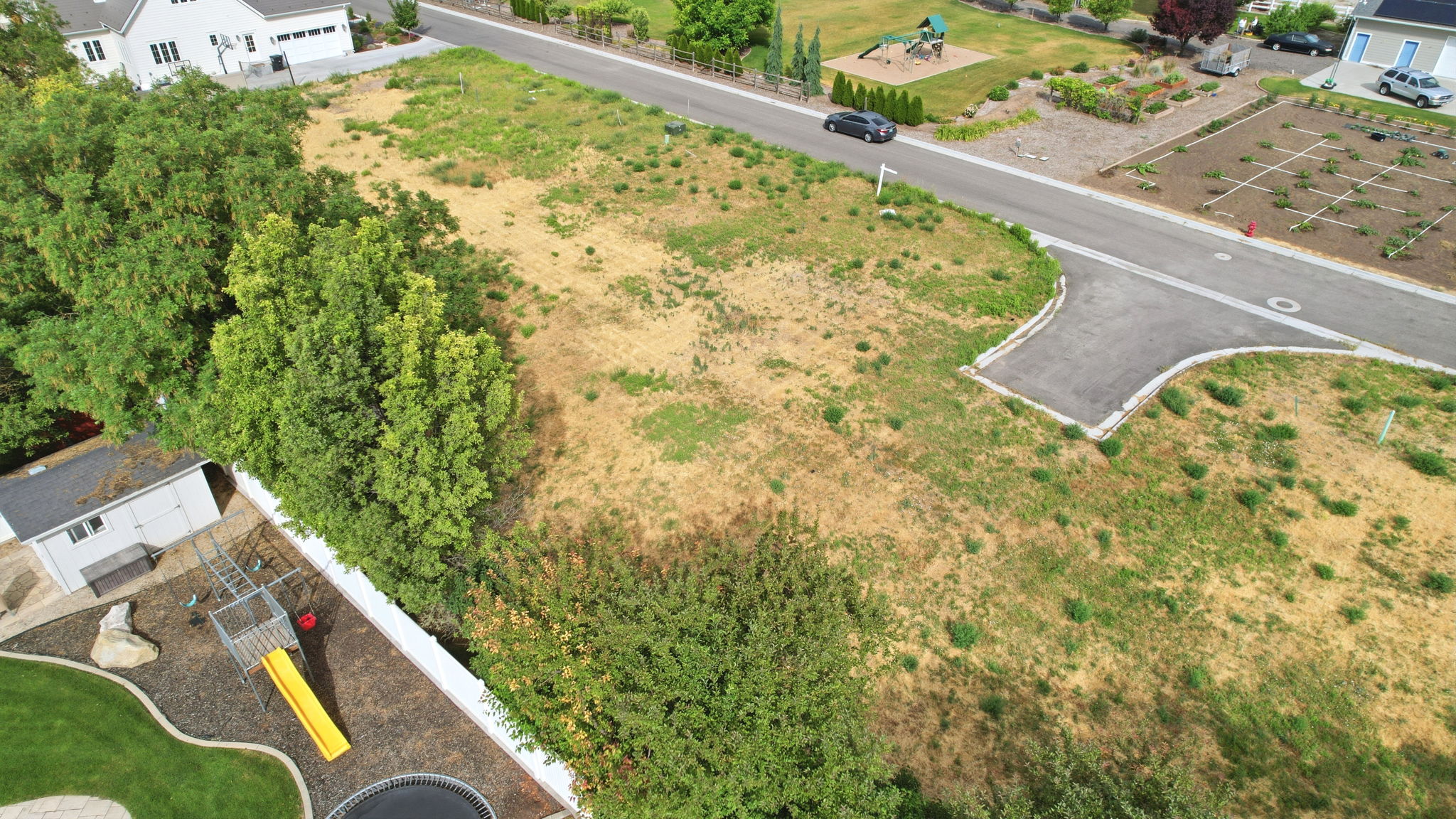 Expansive vacant lot featuring a paved cul-de-sac entrance, mature perimeter trees, and street frontage