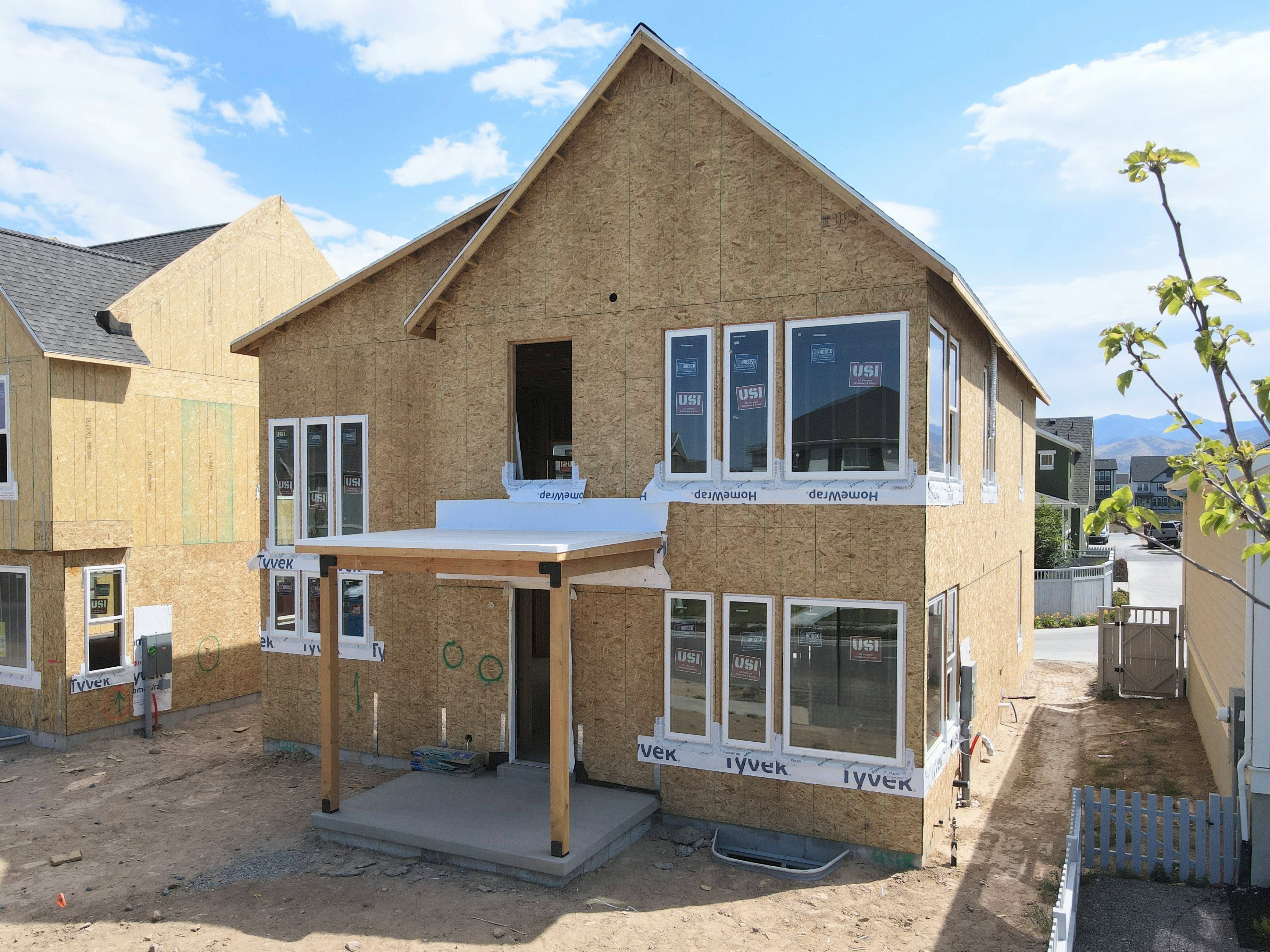 Two-story construction featuring an unfinished exterior and an attached covered patio with wood support beams
