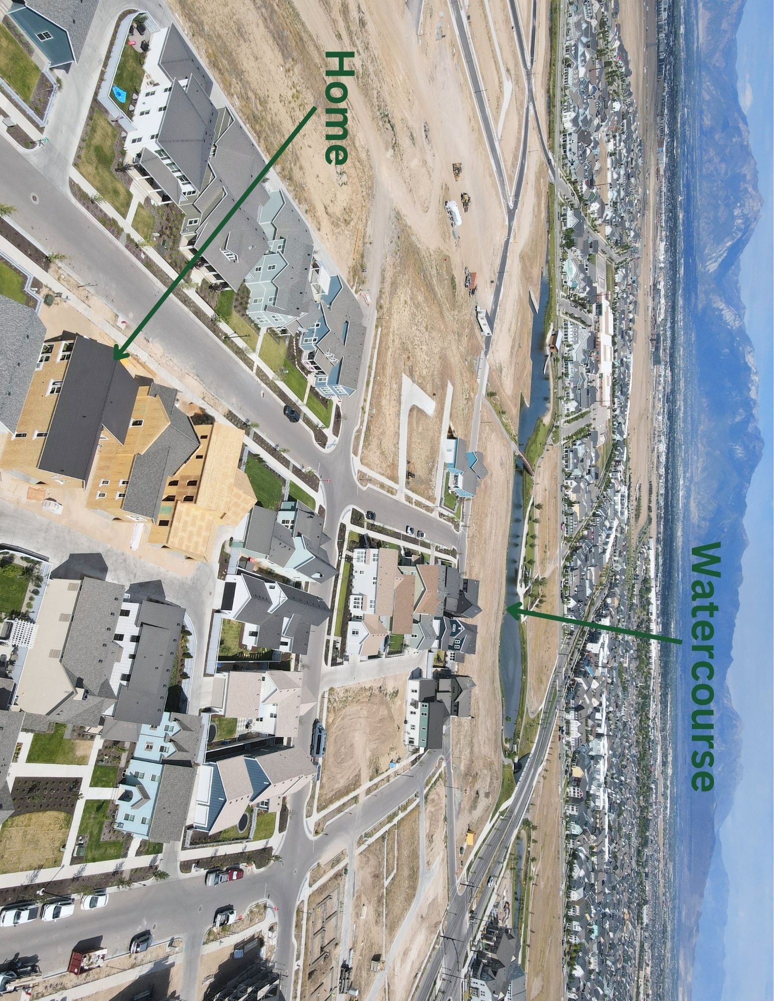 Expansive neighborhood featuring a watercourse, paved streets, and mountain backdrop