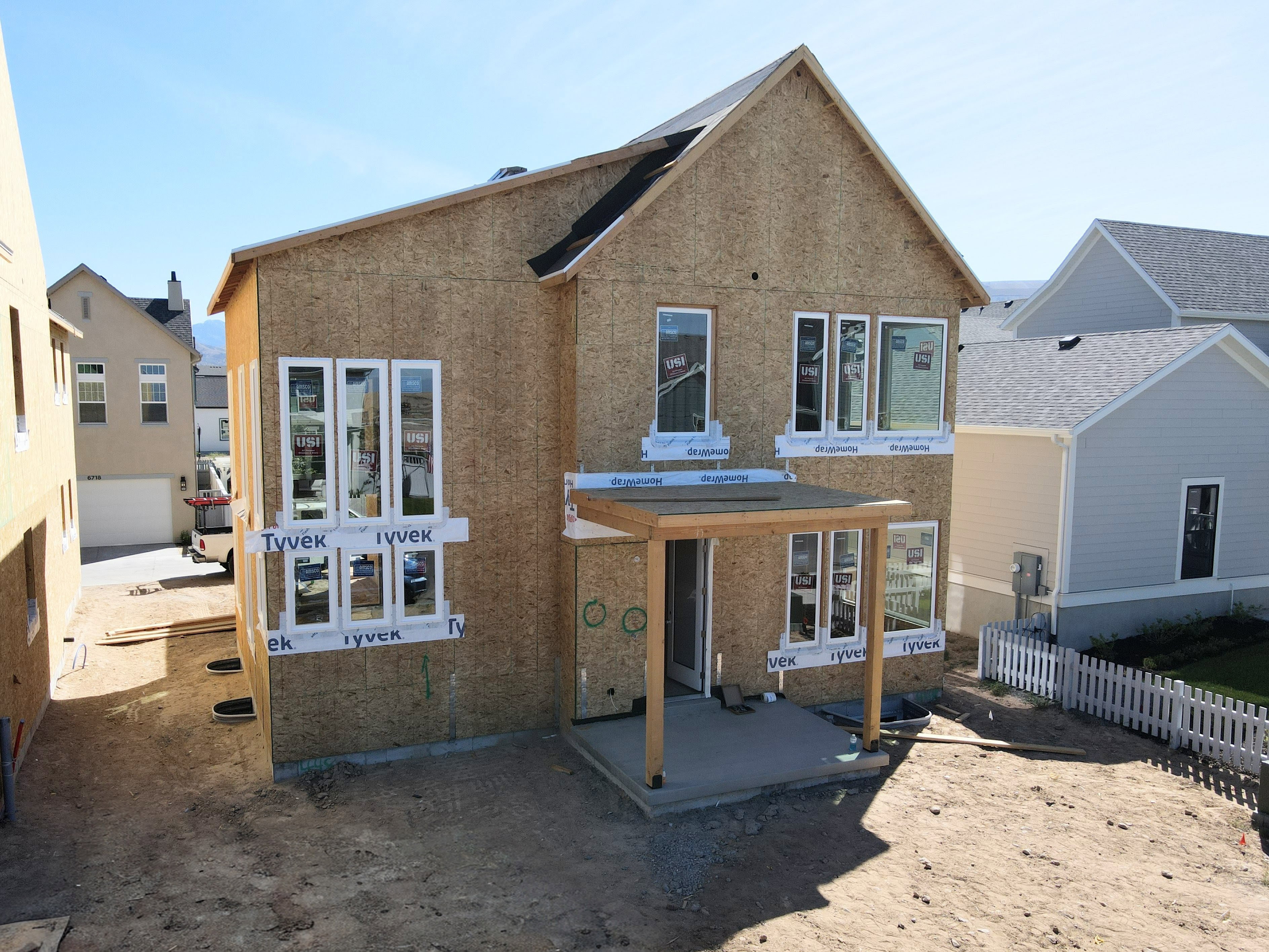 Two-story wood-sheathed structure with multiple windows, a rear patio with a wood pergola, and a partially installed roof