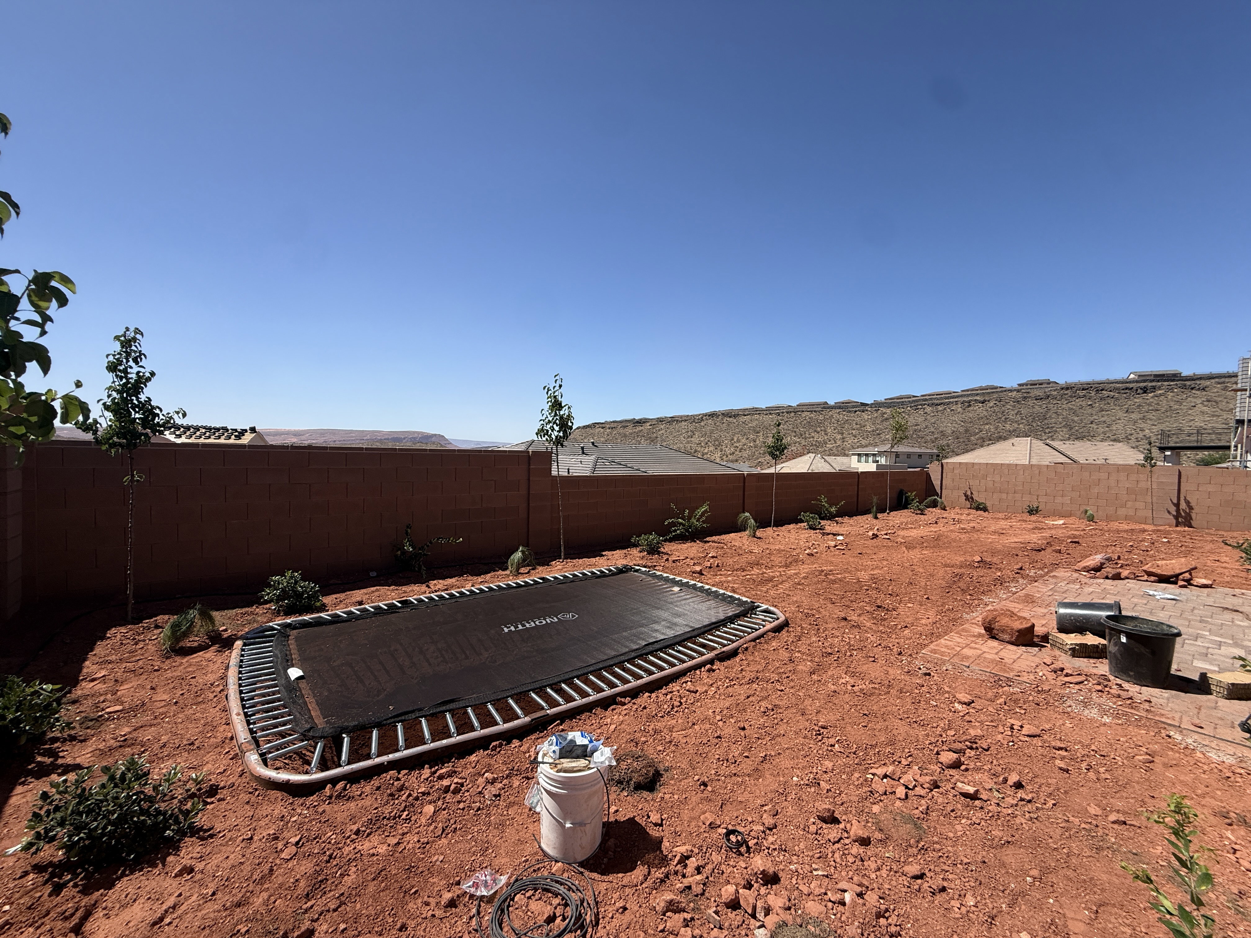 Expansive outdoor area featuring a terracotta-hued landscape, a perimeter block wall, and distant desert hills
