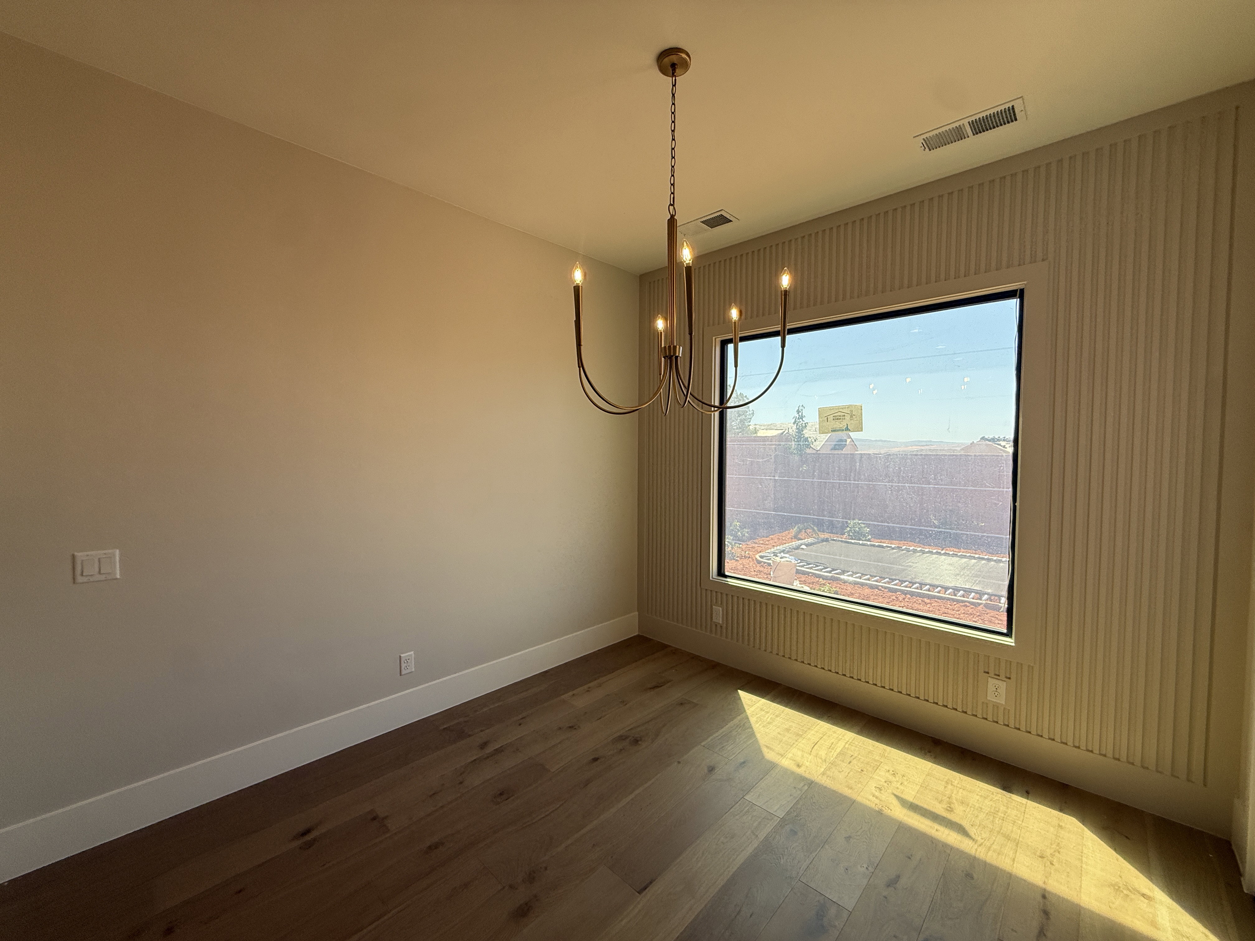 Hardwood-finish flooring complementing a large picture window, a five-light chandelier, and decorative vertical wall paneling