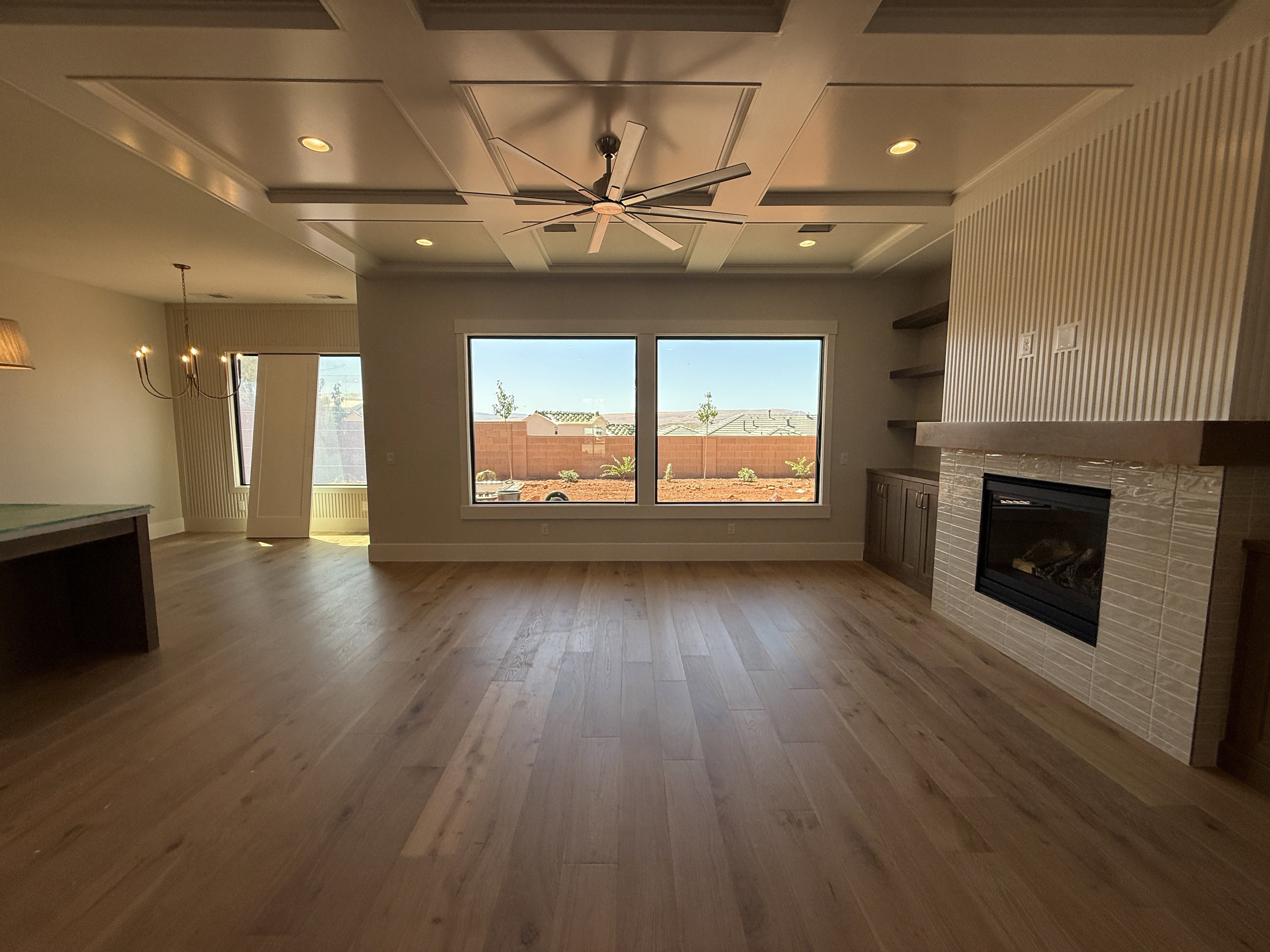 Open-concept living area featuring wood-finish flooring, a coffered ceiling with recessed lighting and a ceiling fan, and large windows