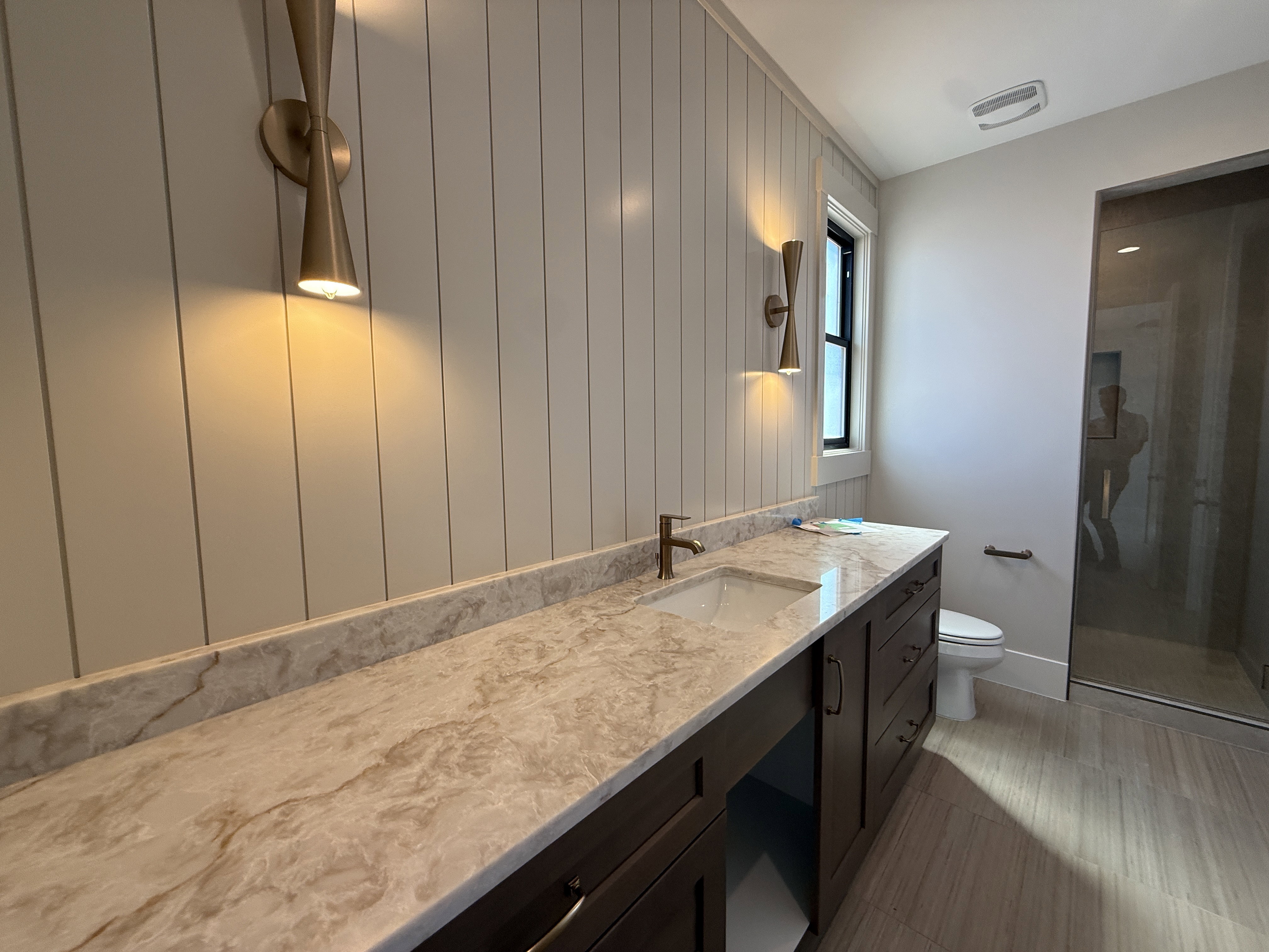 Bathroom featuring a dark wood vanity with ample storage, a light-toned stone-finish countertop with an integrated sink, and brushed brass fixtures