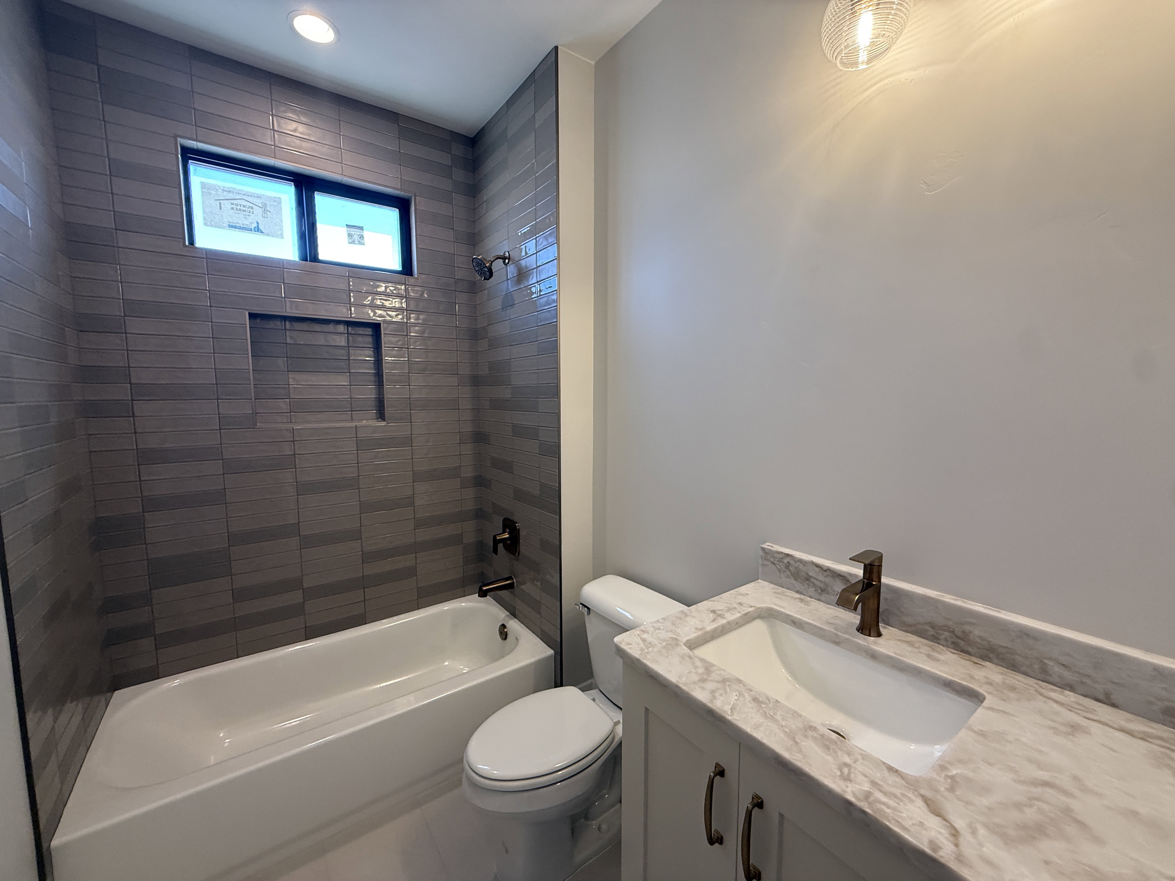 Bathroom featuring a white bathtub, gray tile surround with recessed niche, and a contrasting window