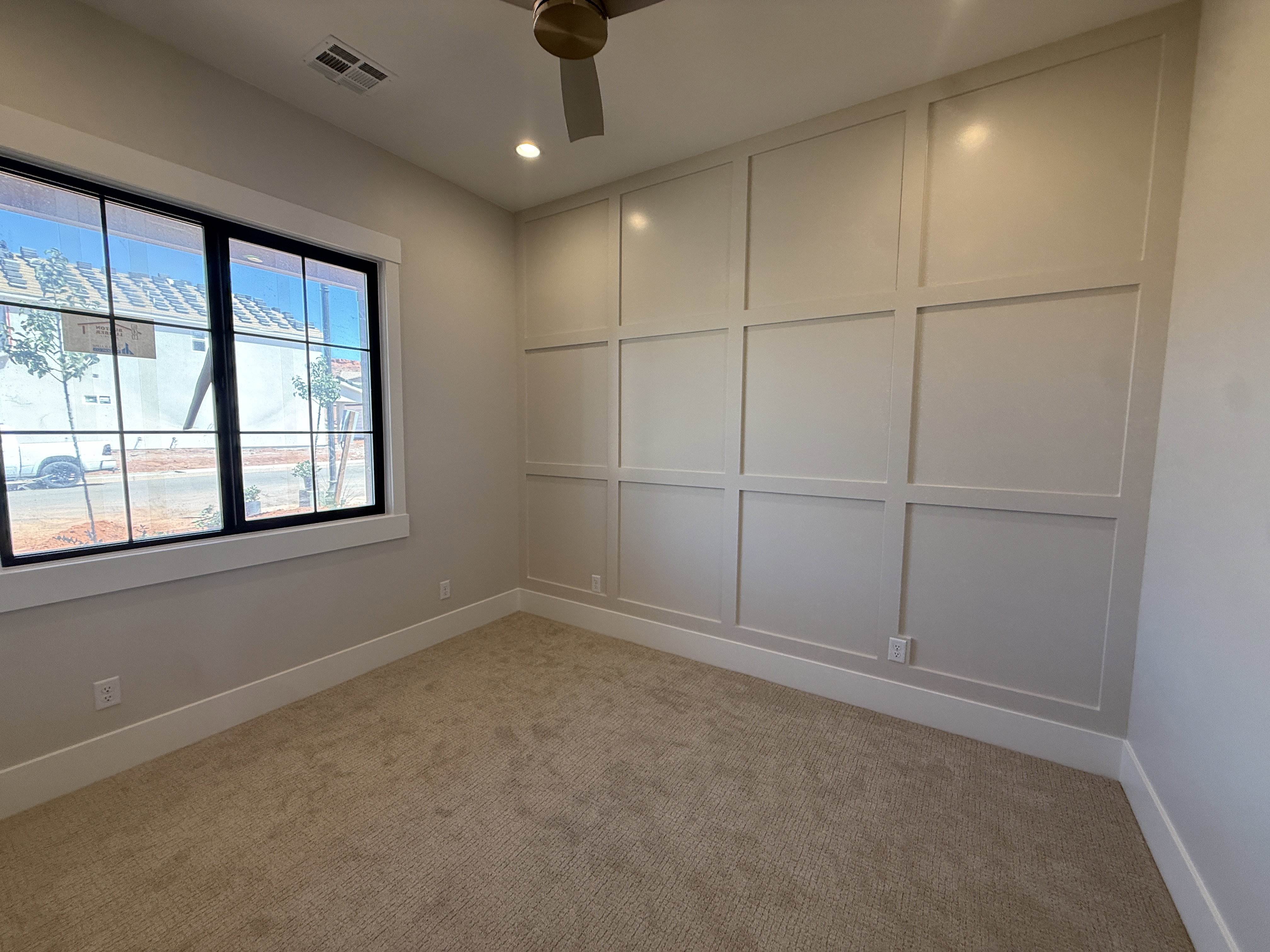 Accent wall with grid paneling, neutral-tone carpeting, window with black trim, recessed lighting, and a ceiling fan