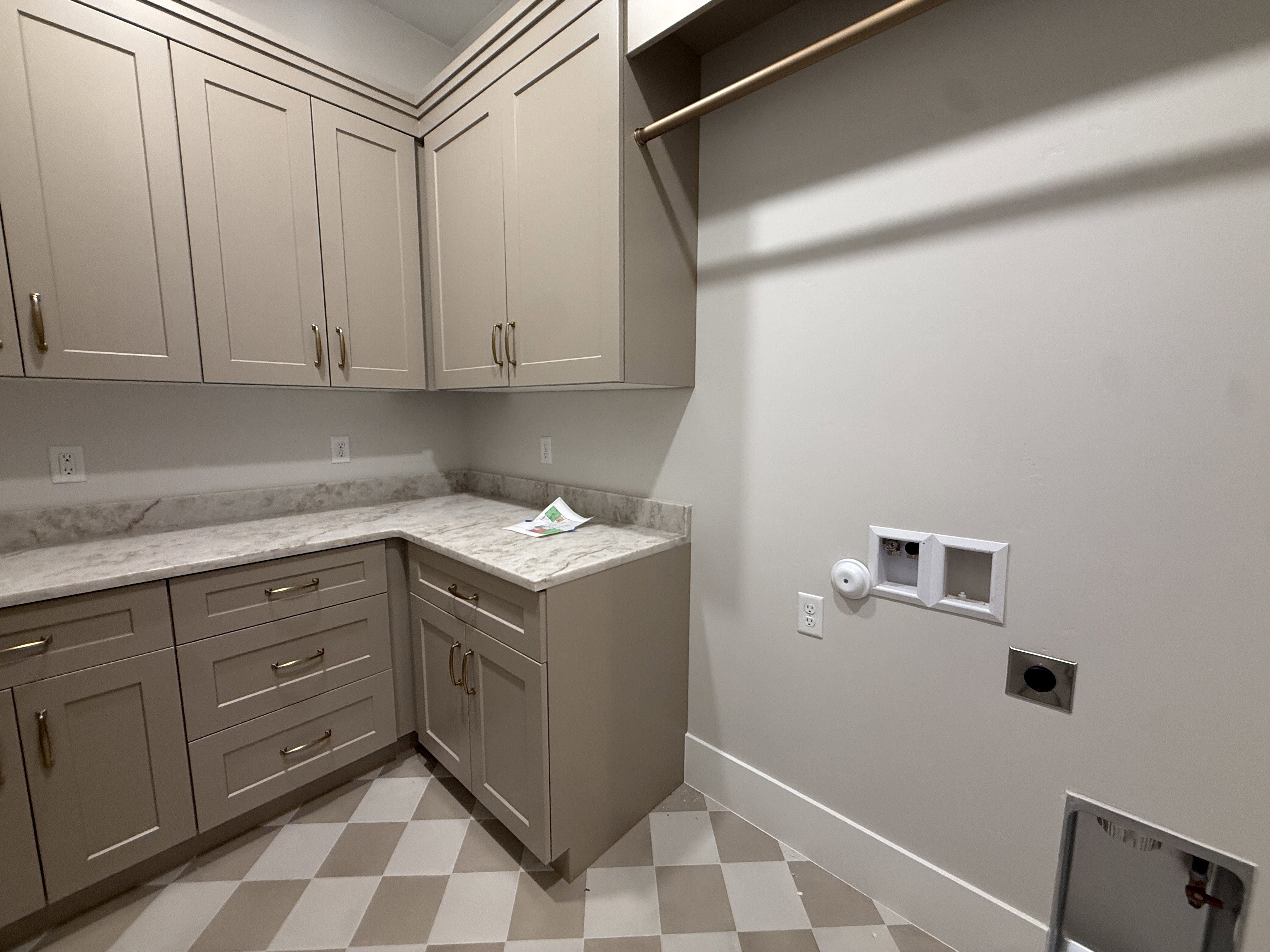 Utility room featuring extensive cabinetry with gold-toned hardware, light-toned stone countertops, and a checkered tile floor