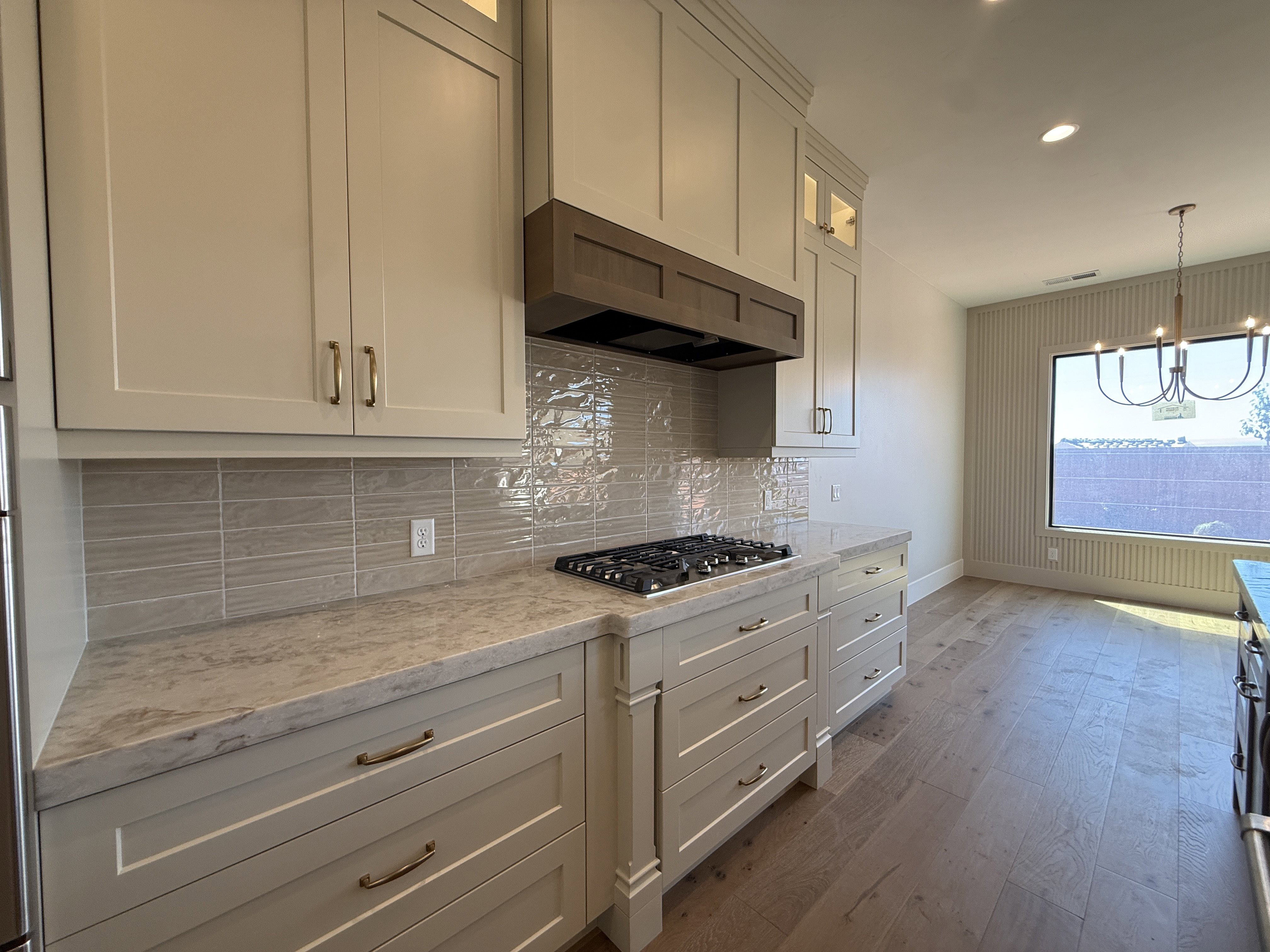 Kitchen featuring light-toned cabinetry with brass hardware, a gas cooktop, and a wood-finish range hood