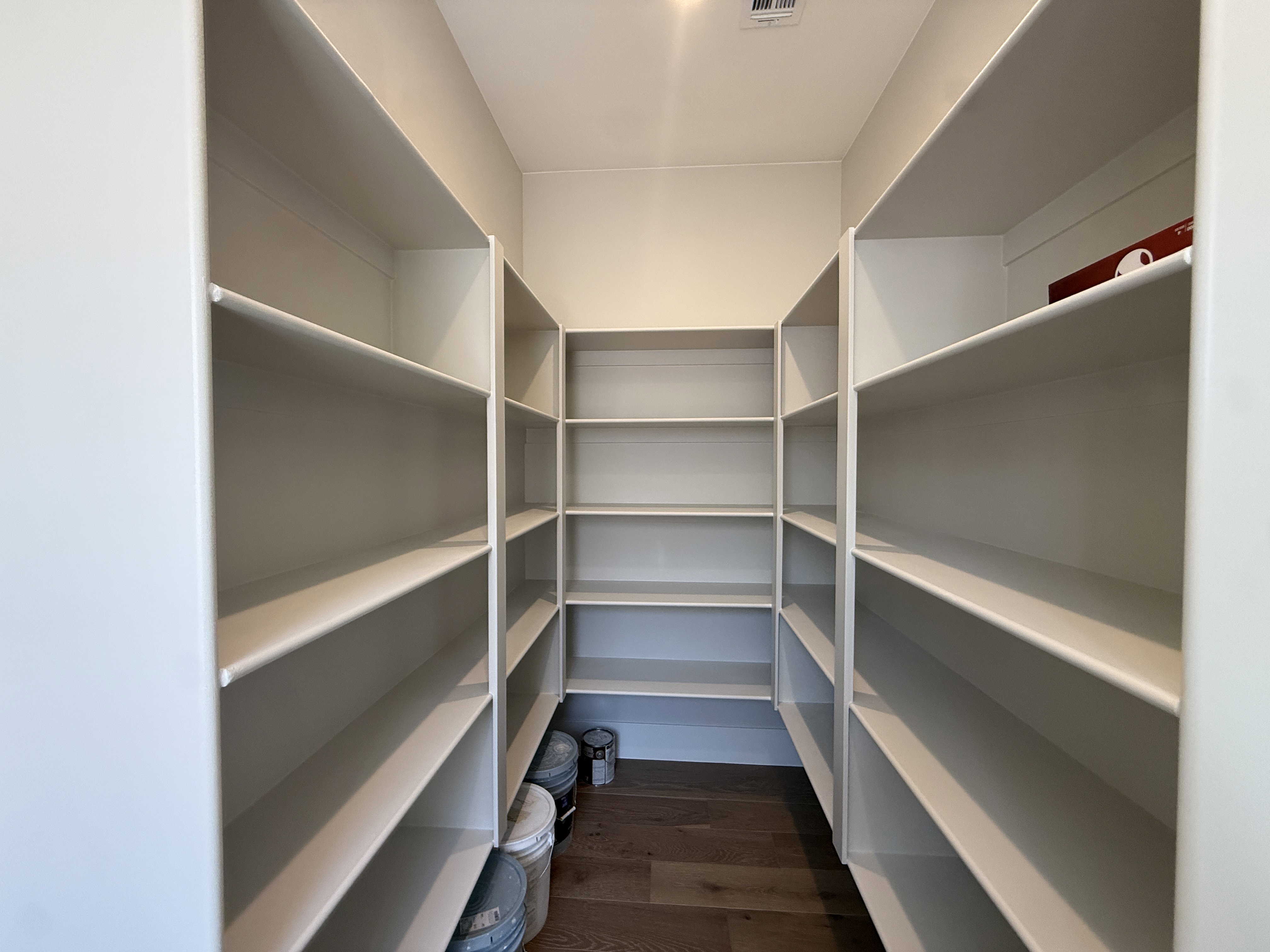 Walk-in pantry featuring extensive white shelving, recessed lighting, and wood-finish flooring