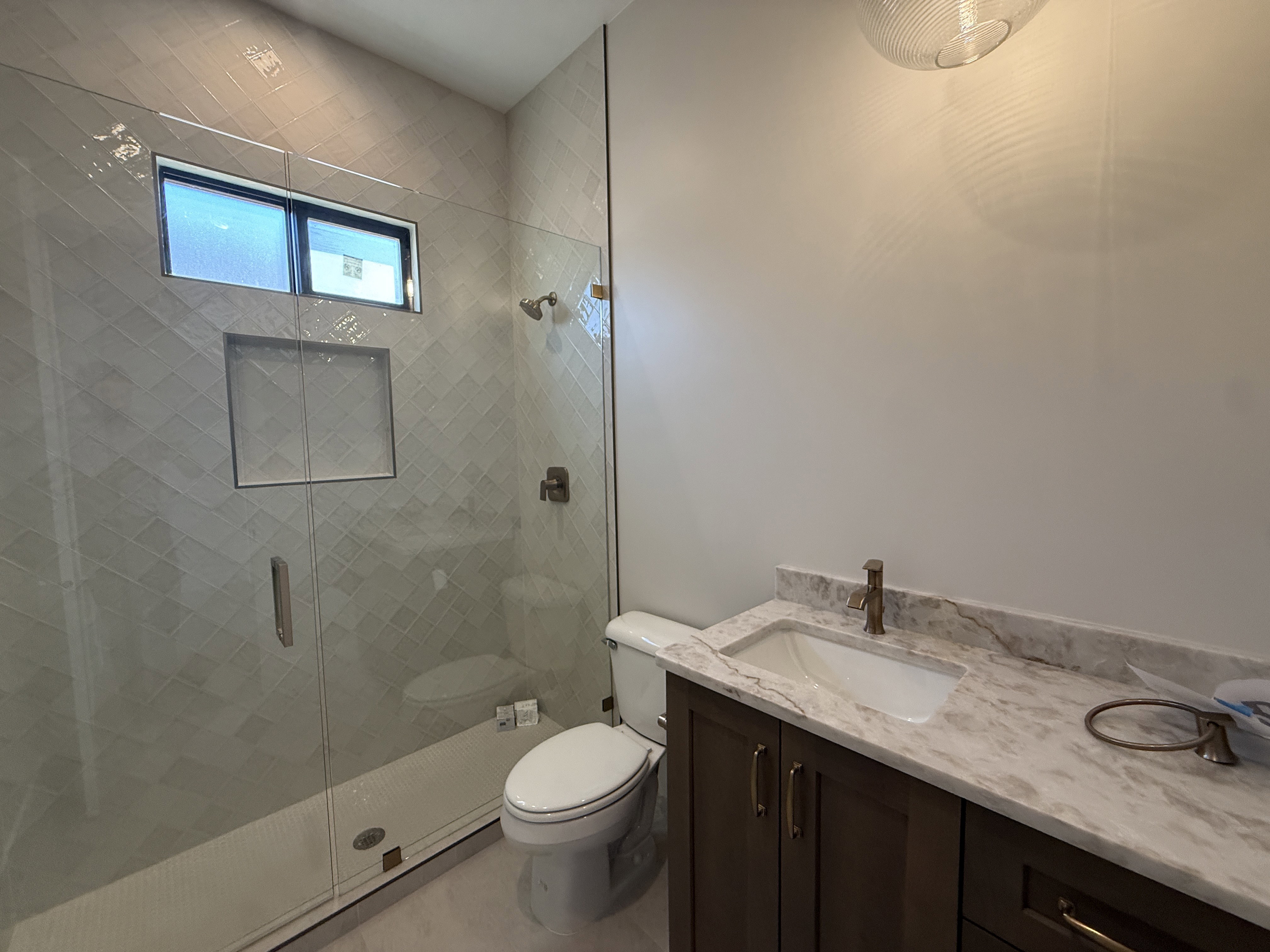 Bathroom featuring a glass-enclosed shower with herringbone tile, an integrated shower niche, and a transom window