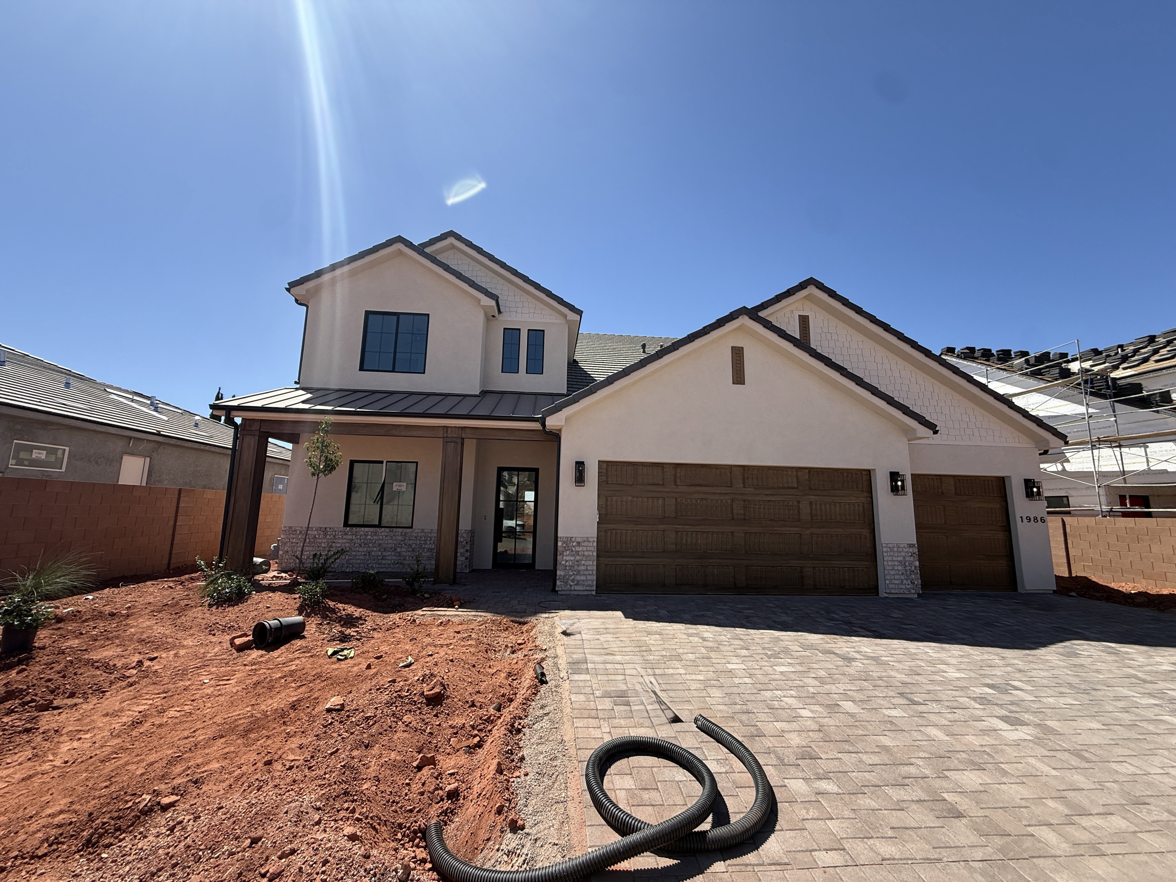 Contemporary stucco exterior with stone accents, featuring a covered entry, dark-framed windows, a patterned paver driveway, and two wood-finish garage doors