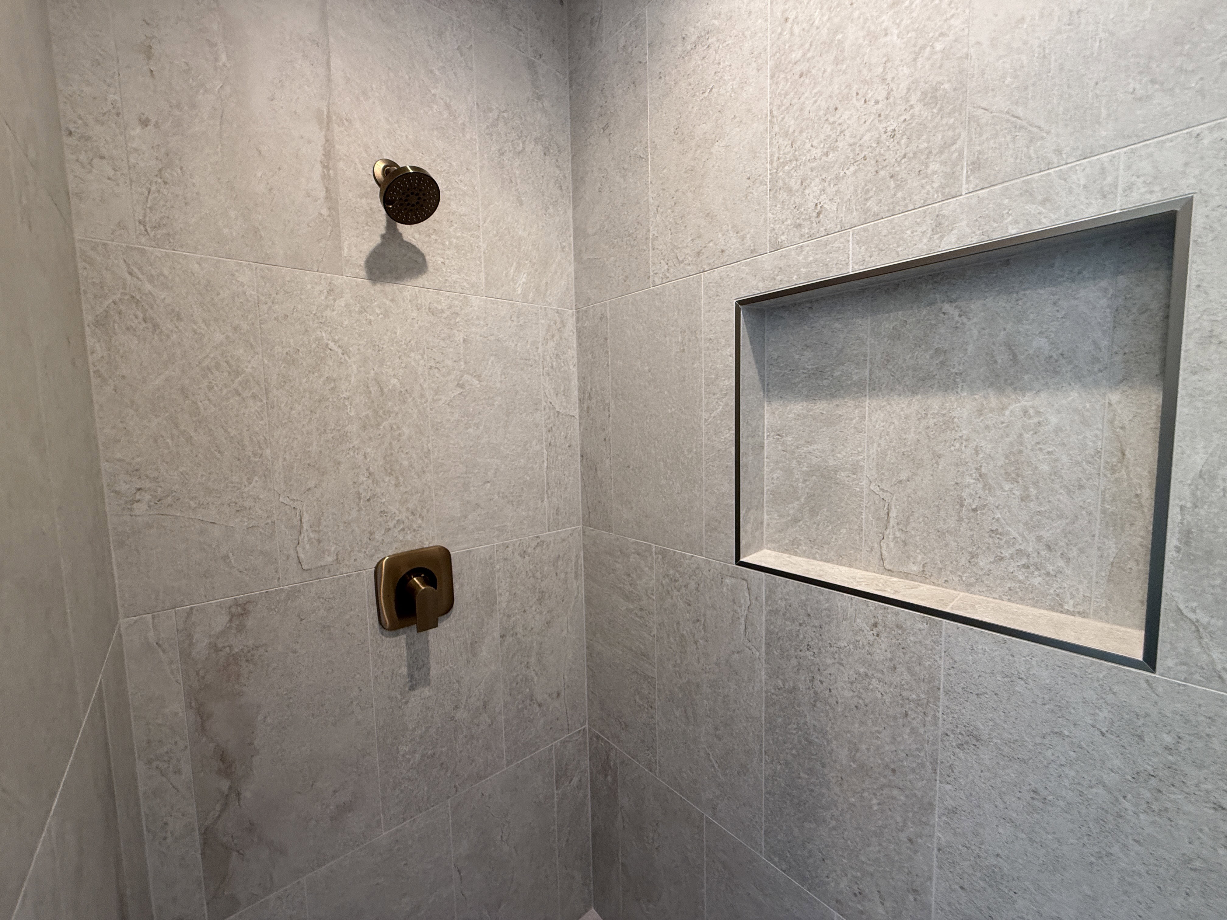 Shower enclosure featuring textured gray tile, a built-in recessed niche, and bronze fixtures
