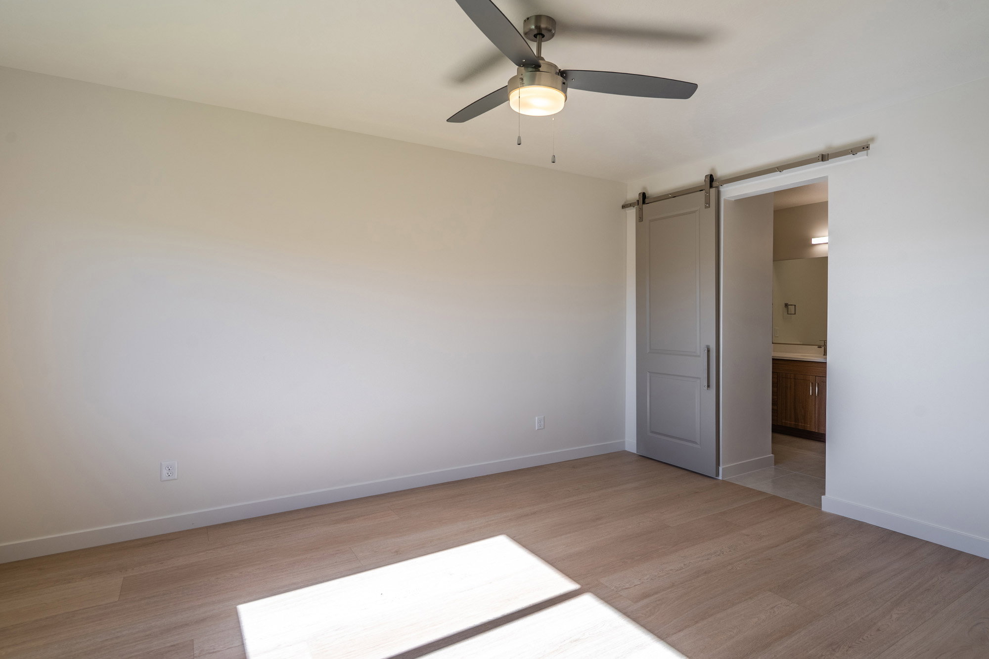 Unfurnished bedroom with a barn door, light wood-style flooring, a ceiling fan, and connected bathroom