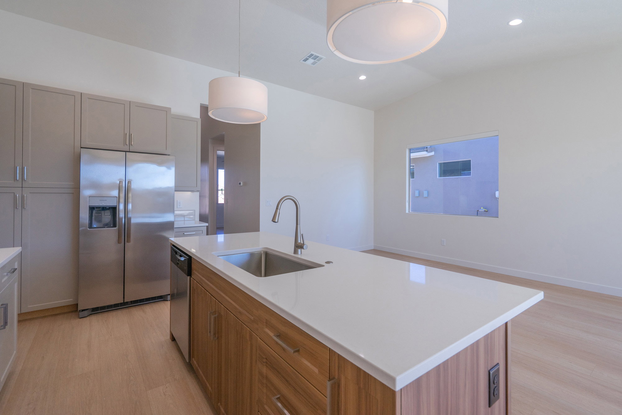 Kitchen with stainless steel appliances, light wood-style floors, vaulted ceiling, an island with sink, and decorative light fixtures