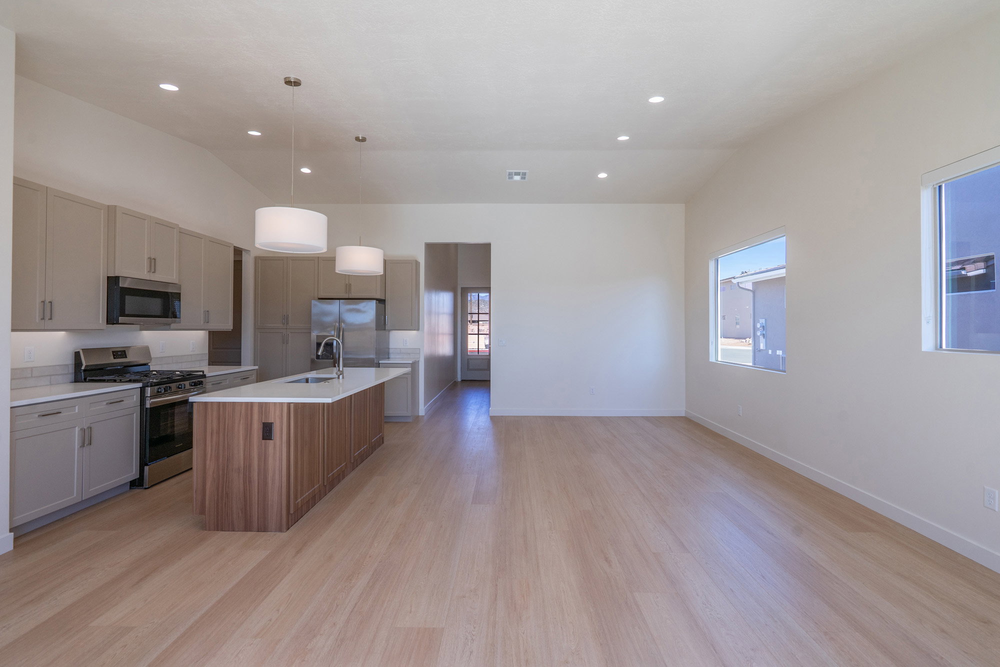 Two tone kitchen with vaulted ceiling, stainless steel appliances, open floor plan, a kitchen island with sink, and light wood-style flooring
