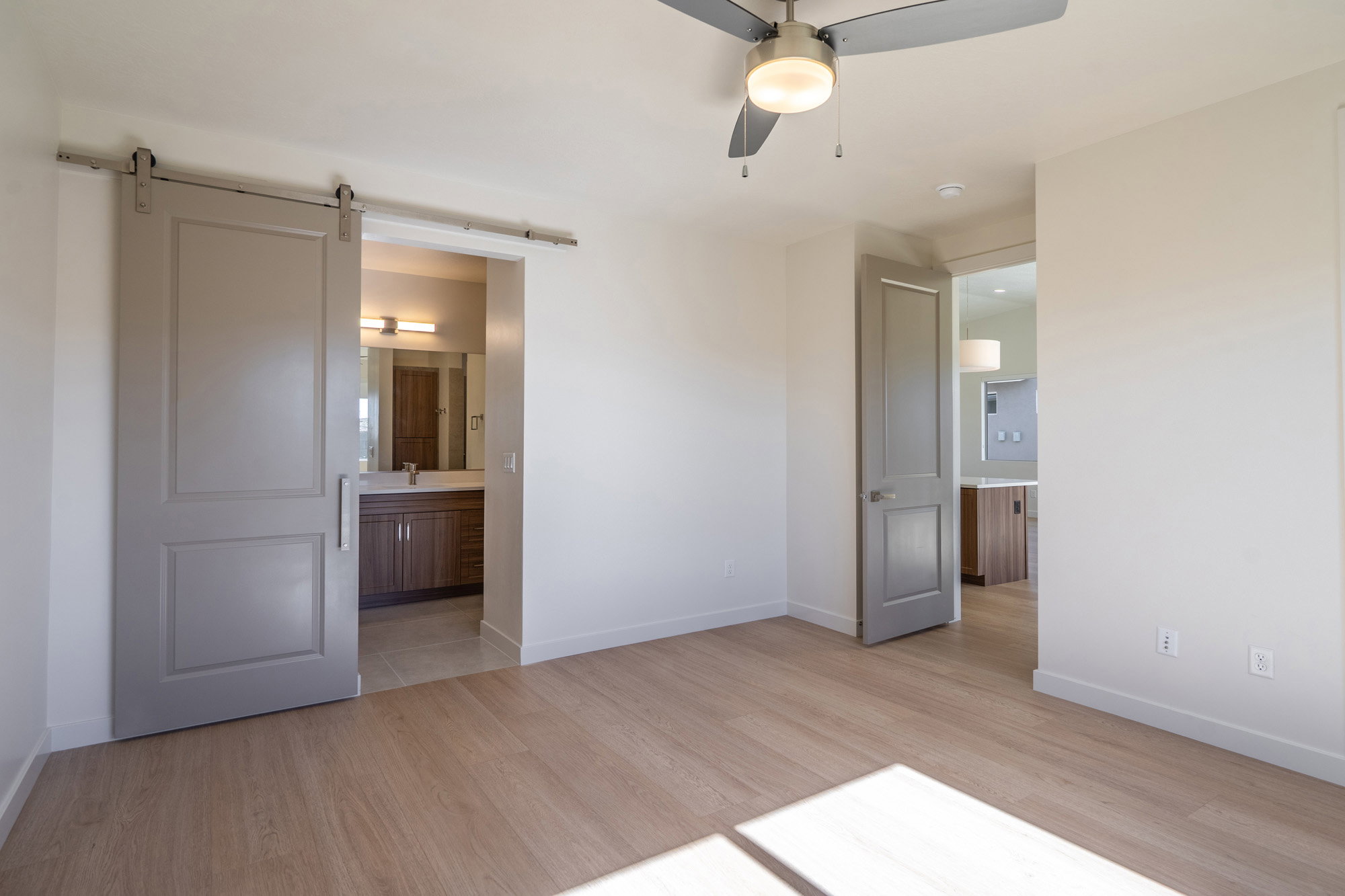 Unfurnished bedroom with a barn door, light wood-style flooring, a ceiling fan, and connected bathroom