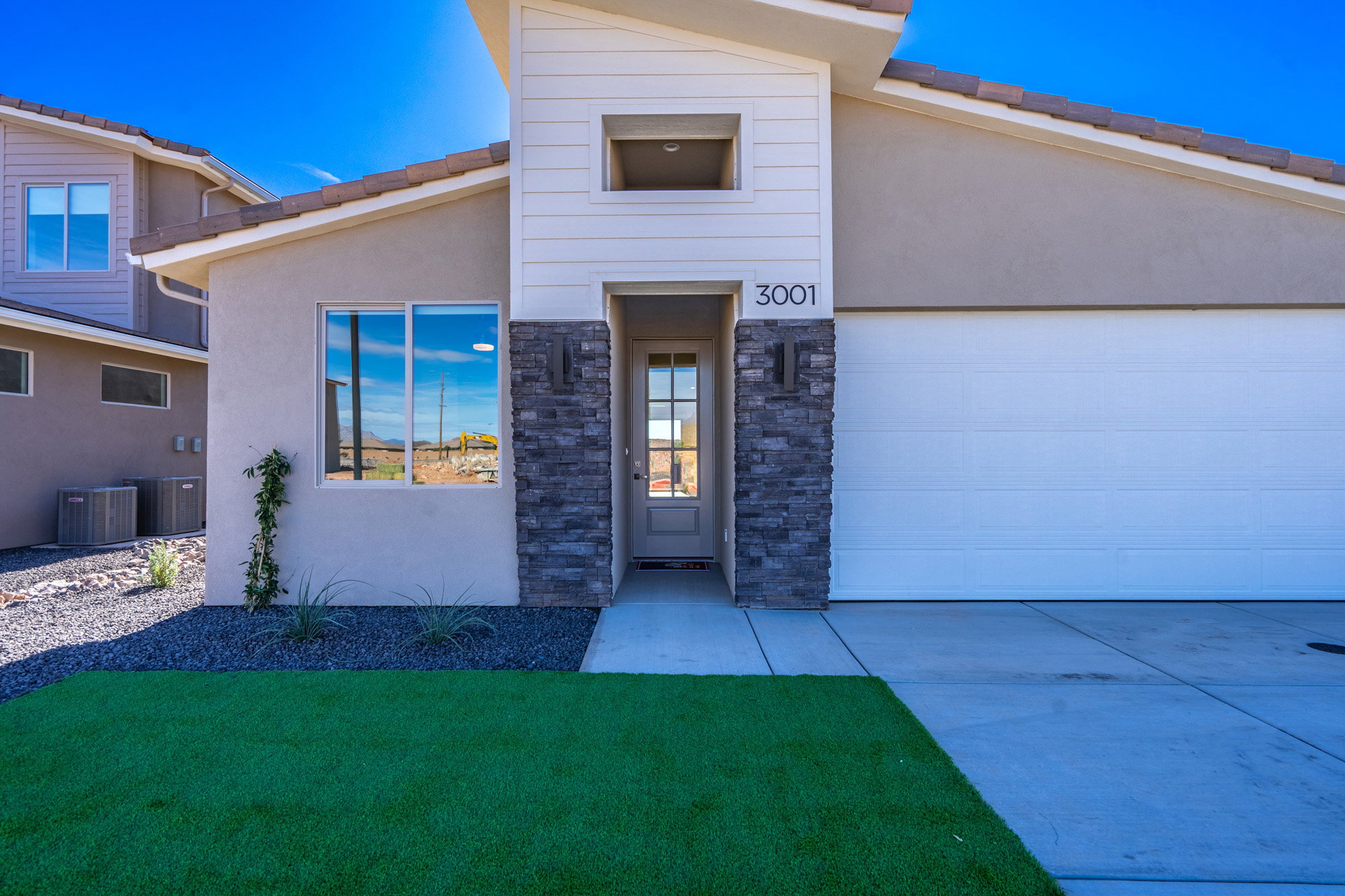 View of front of home featuring stucco siding, stone siding, driveway, a tile roof, and a front yard