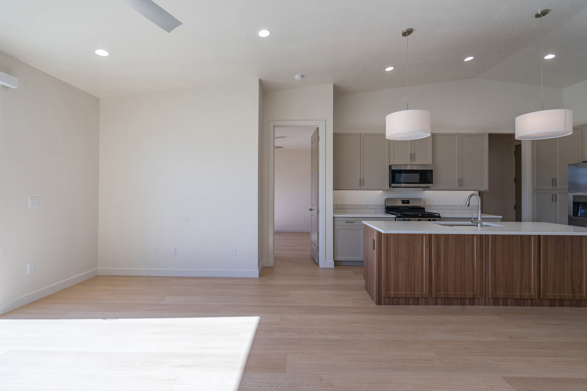 Kitchen featuring an island with sink, stainless steel appliances, decorative light fixtures, light wood-style floors, and open floor plan